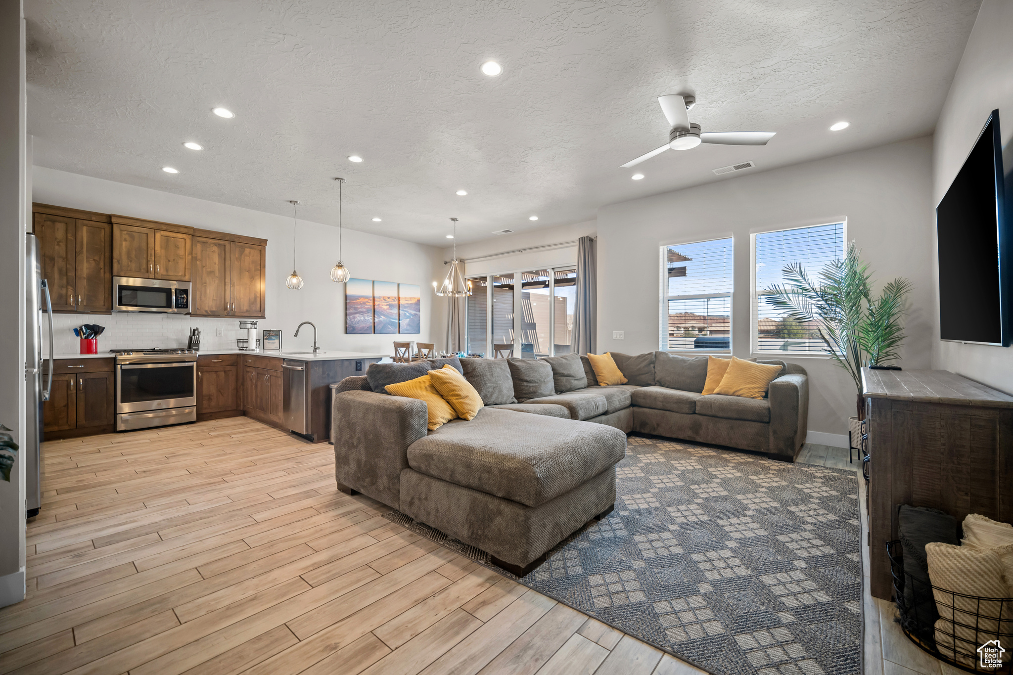 Living room with sink, light wood-type flooring, ceiling fan with notable chandelier, and a textured ceiling