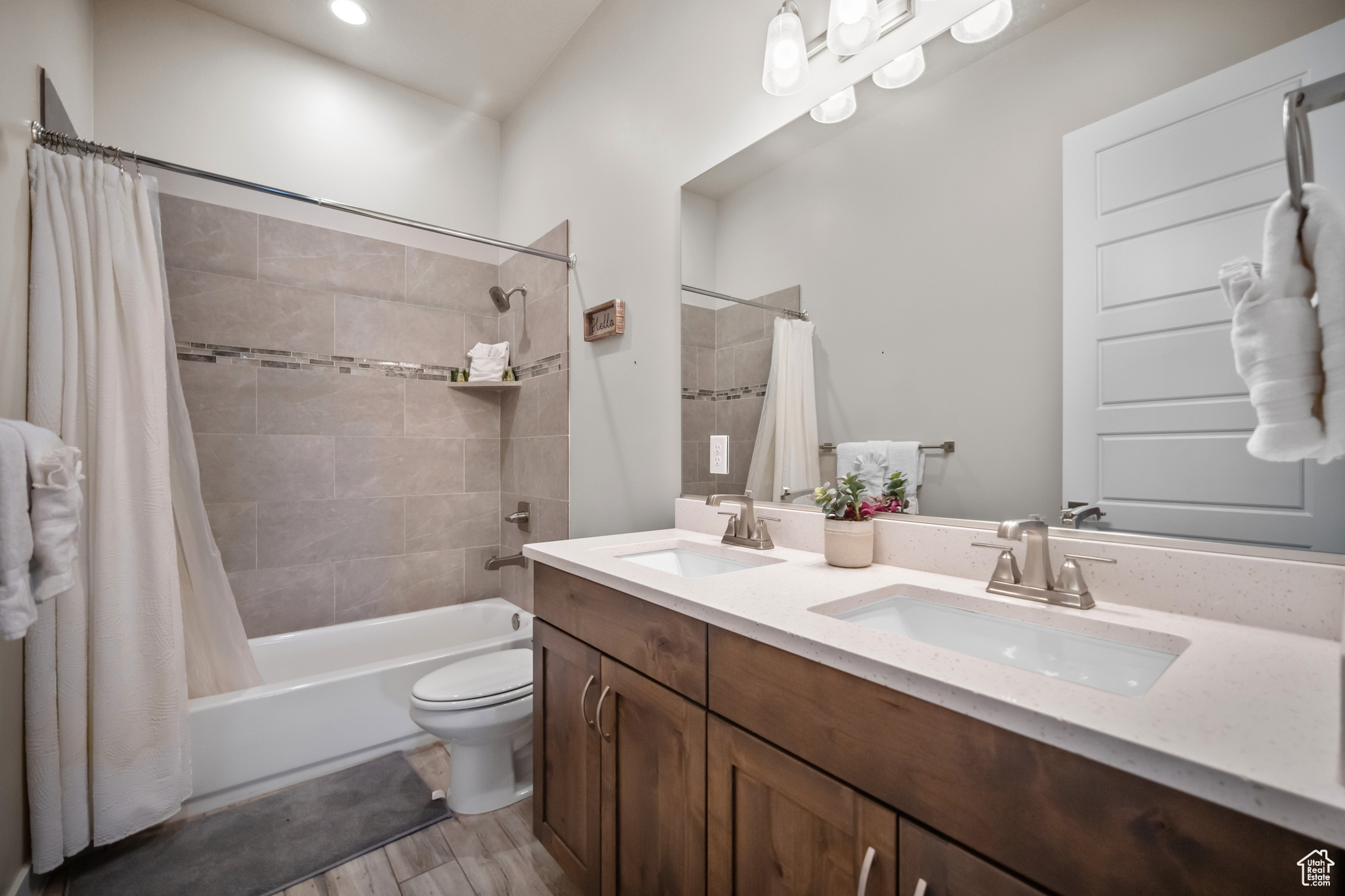 Full bathroom featuring hardwood / wood-style floors, shower / bath combo with shower curtain, dual vanity, and toilet