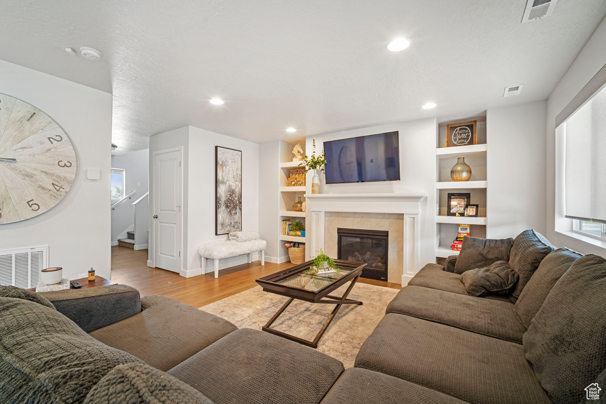 Living room with built in shelves, a wealth of natural light, a tile fireplace, and light wood-type flooring