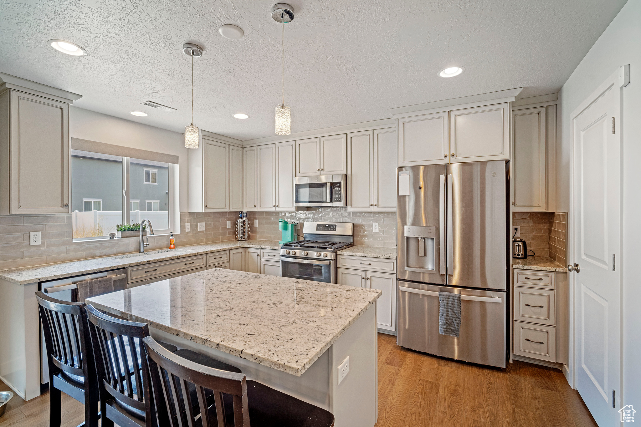 Kitchen with stainless steel appliances, sink, hanging light fixtures, light hardwood / wood-style floors, and backsplash