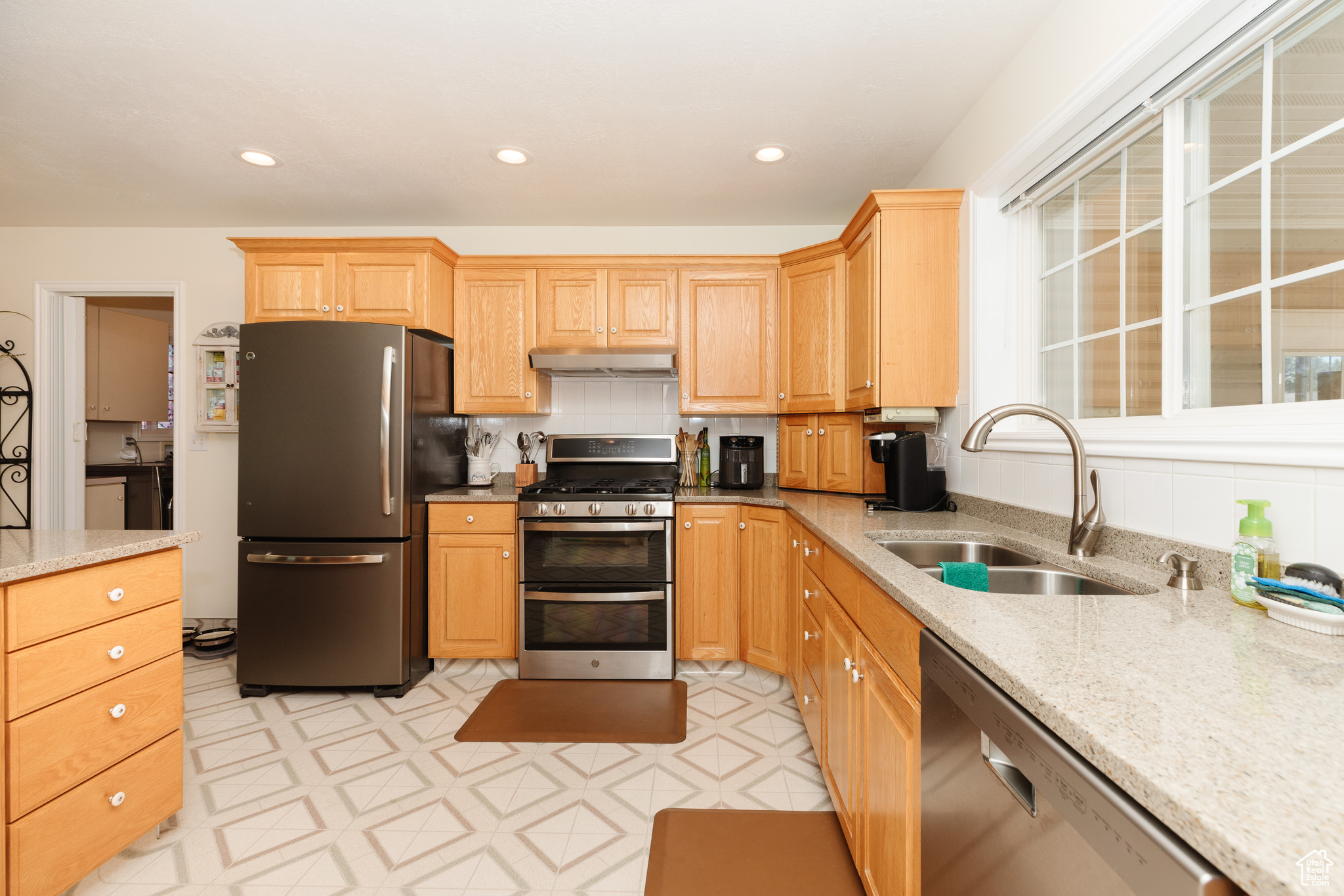 Kitchen with light tile patterned flooring, tasteful backsplash, stainless steel appliances, sink, and light stone counters