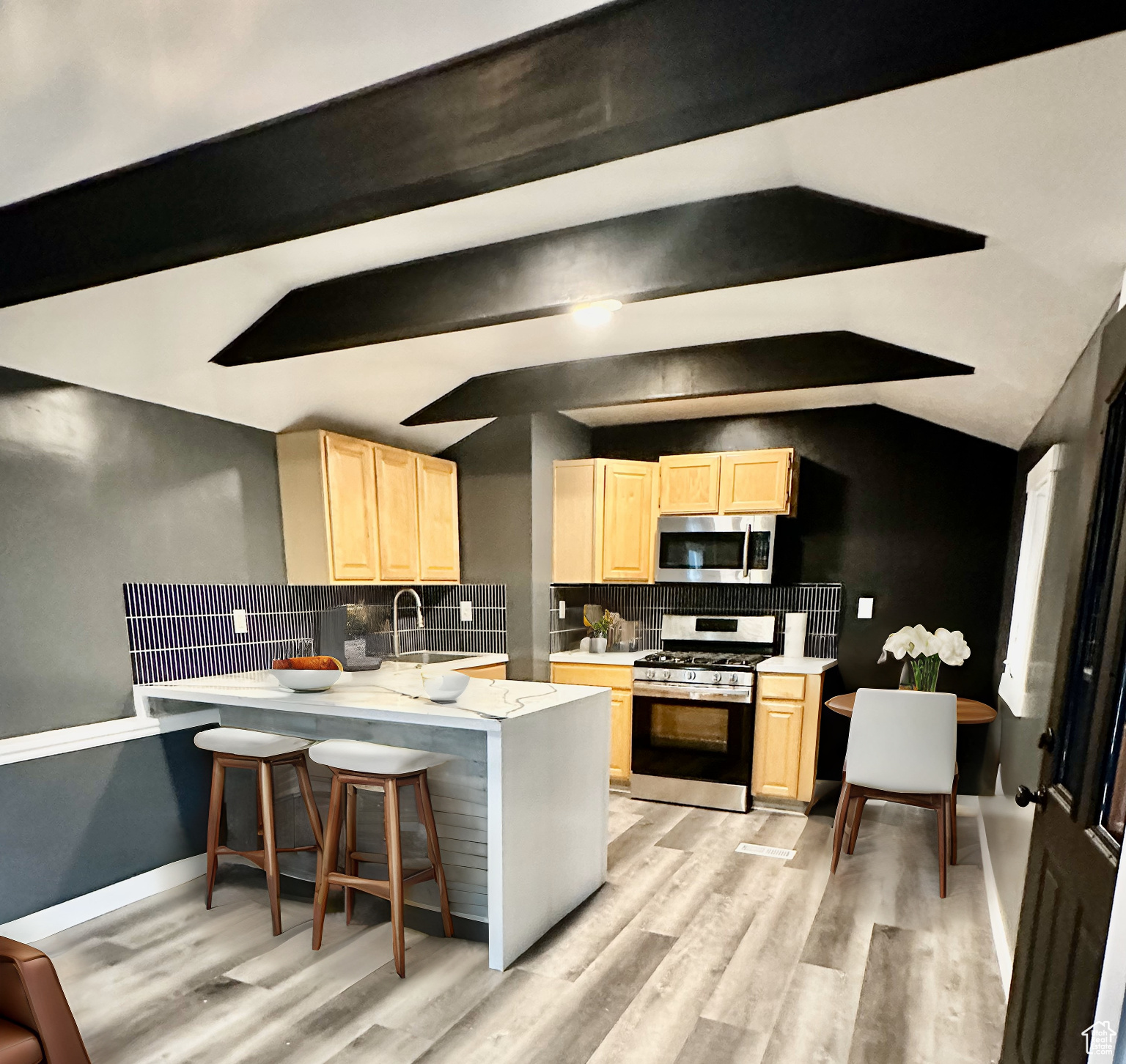 Virtually staged. Kitchen with light brown cabinetry, decorative backsplash, appliances with stainless steel finishes, and vaulted ceiling with beams