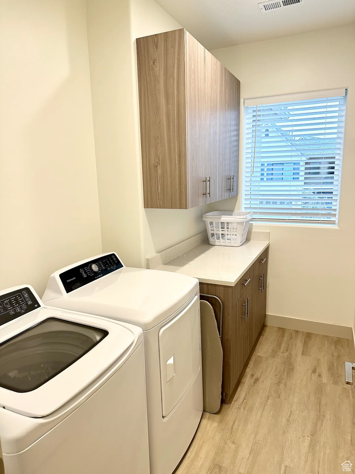 Clothes washing area with cabinets, independent washer and dryer, and light hardwood / wood-style flooring