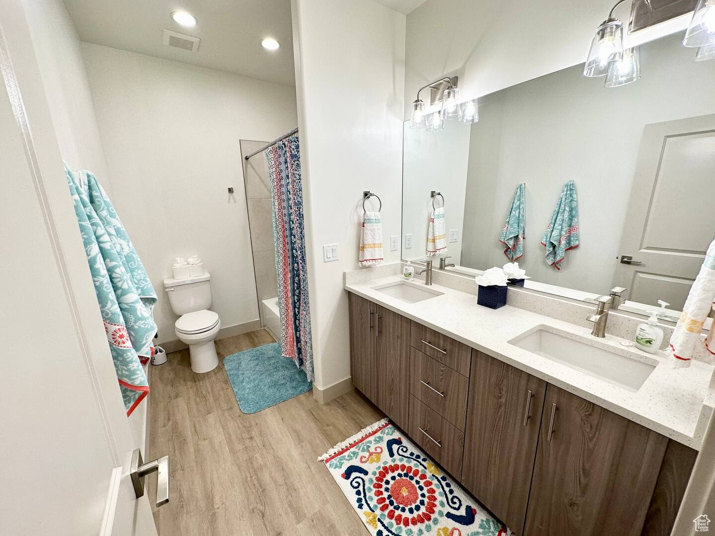 Full bathroom with toilet, wood-type flooring, dual bowl vanity, and shower / bath combination with curtain