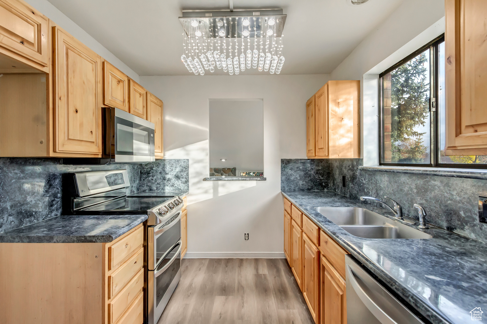 Kitchen featuring appliances with stainless steel finishes, backsplash, sink, pendant lighting, and light hardwood / wood-style flooring