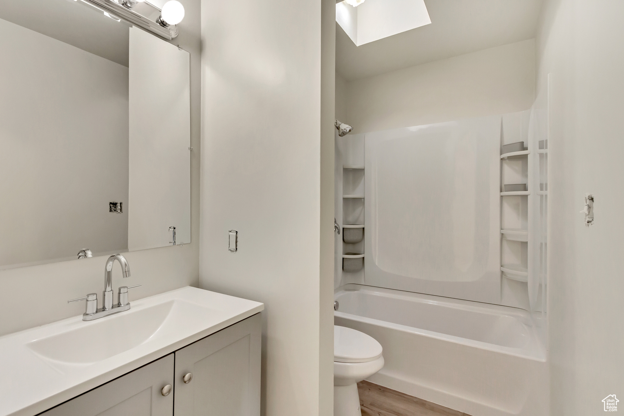 Full bathroom featuring hardwood / wood-style floors, vanity, a skylight, toilet, and shower / bathtub combination