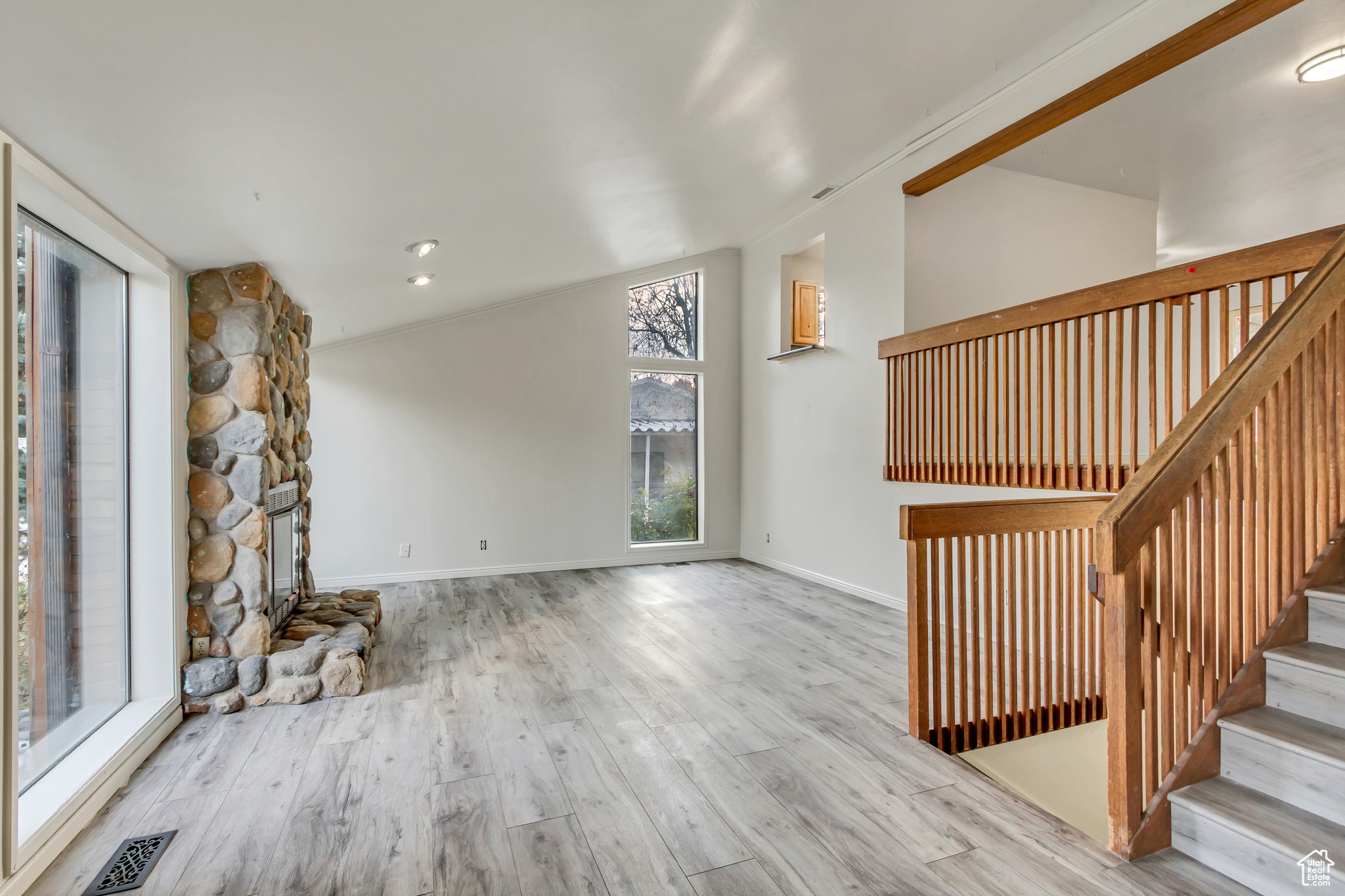 Unfurnished living room with a fireplace, light wood-type flooring, vaulted ceiling, and plenty of natural light