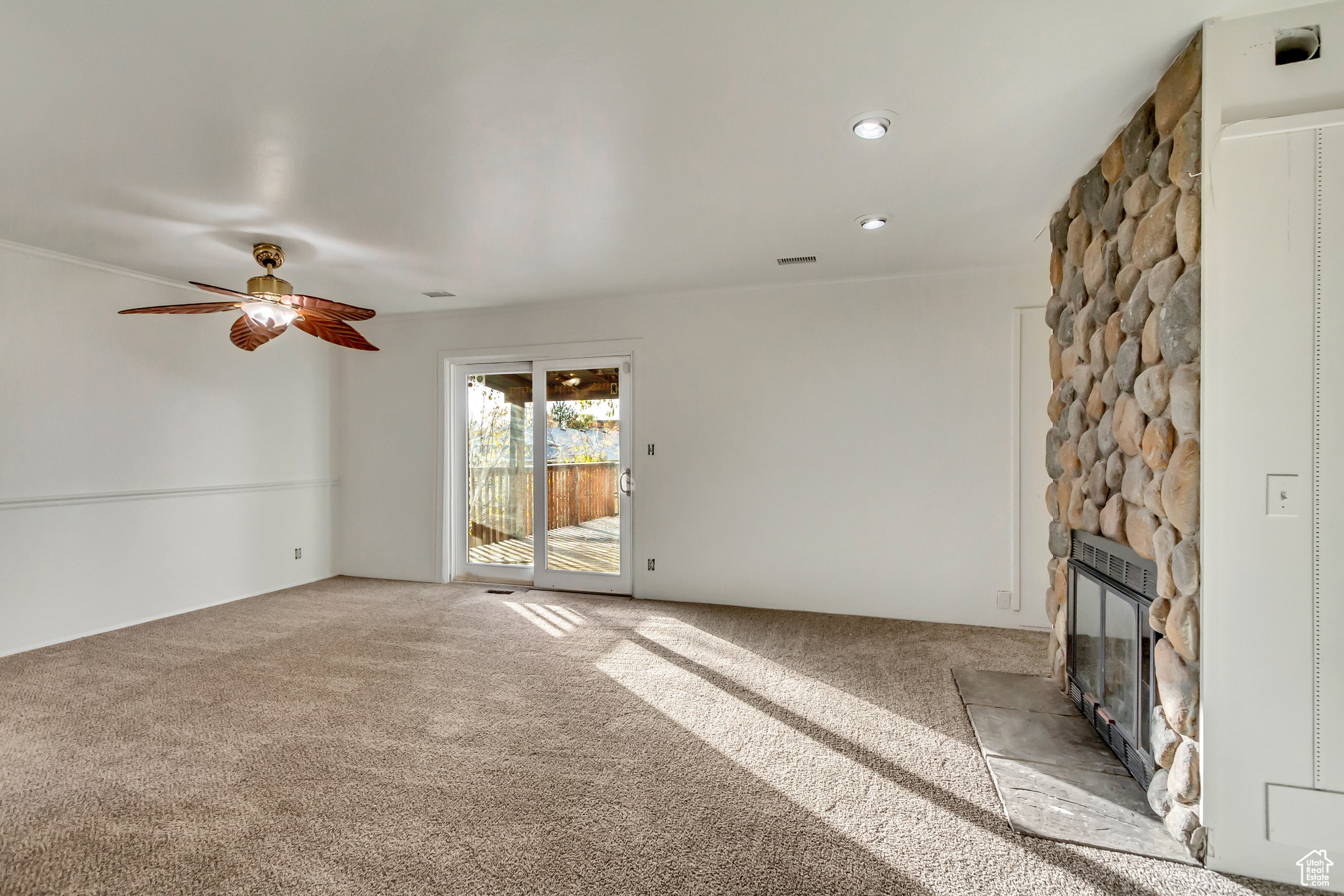 Unfurnished living room featuring carpet flooring, ceiling fan, and a fireplace