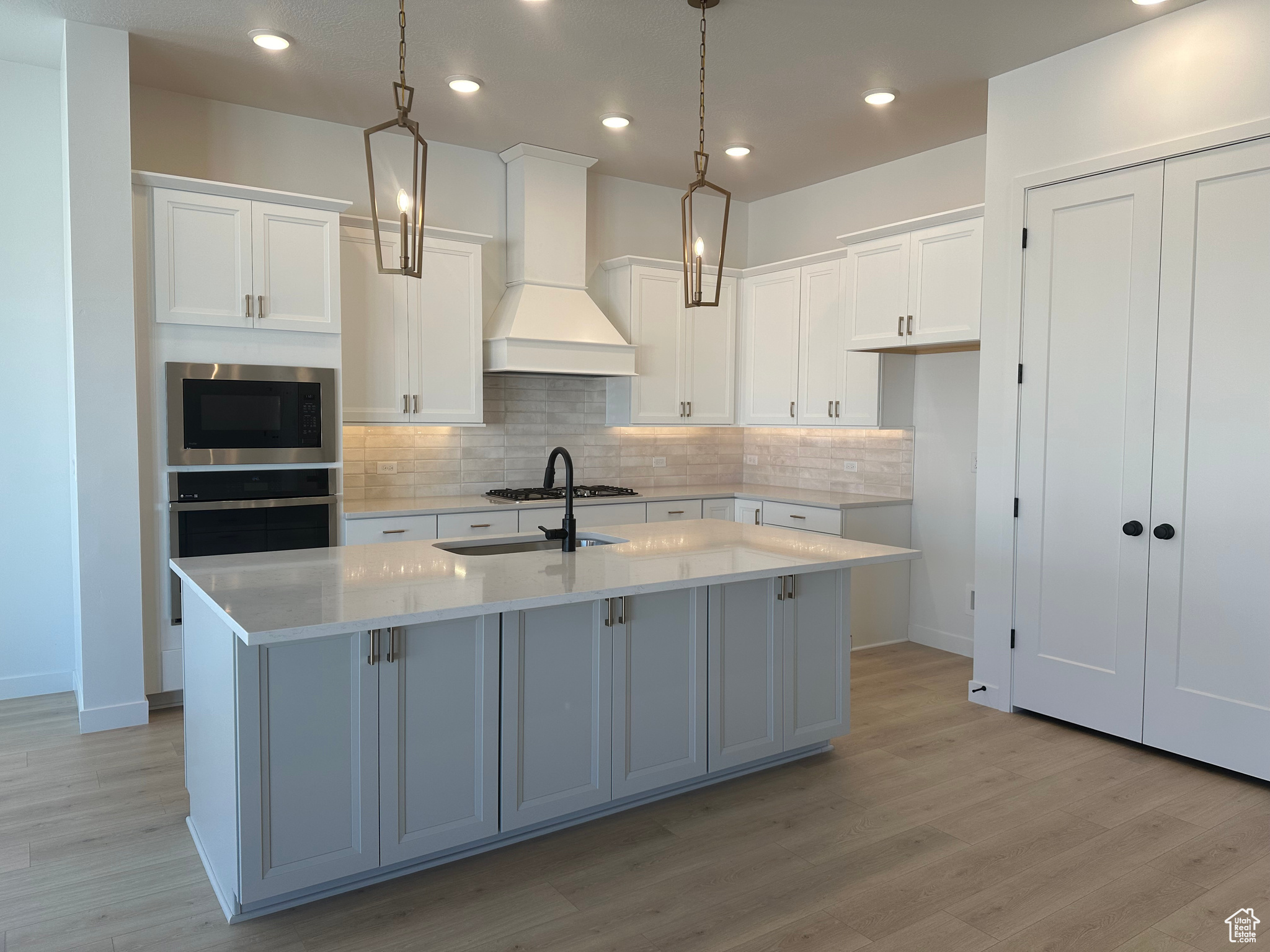 Kitchen with custom range hood, an island with sink, pendant lighting, and stainless steel appliances