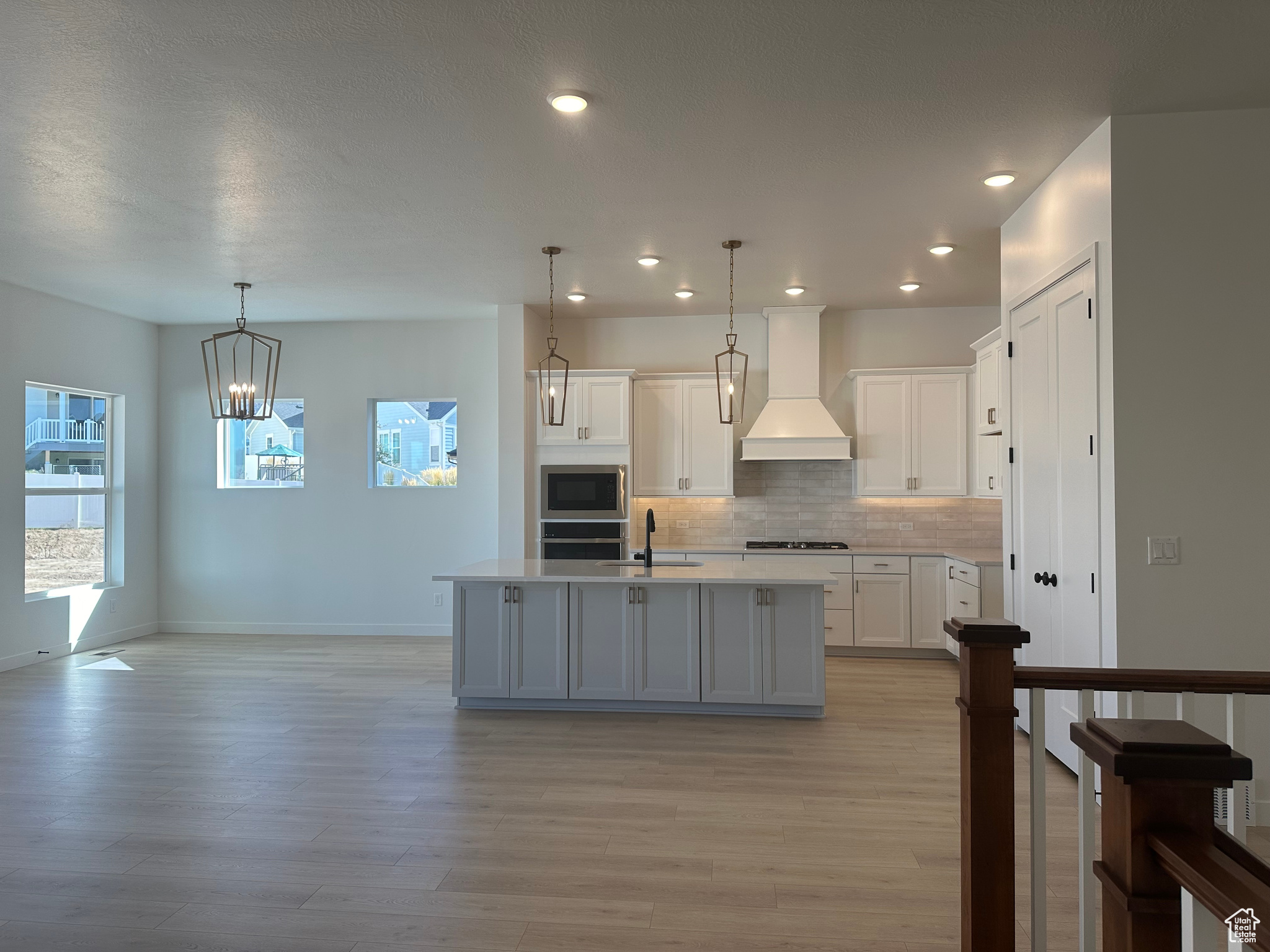 Kitchen with pendant lighting, white cabinets, stainless steel appliances, a center island with sink, and premium range hood