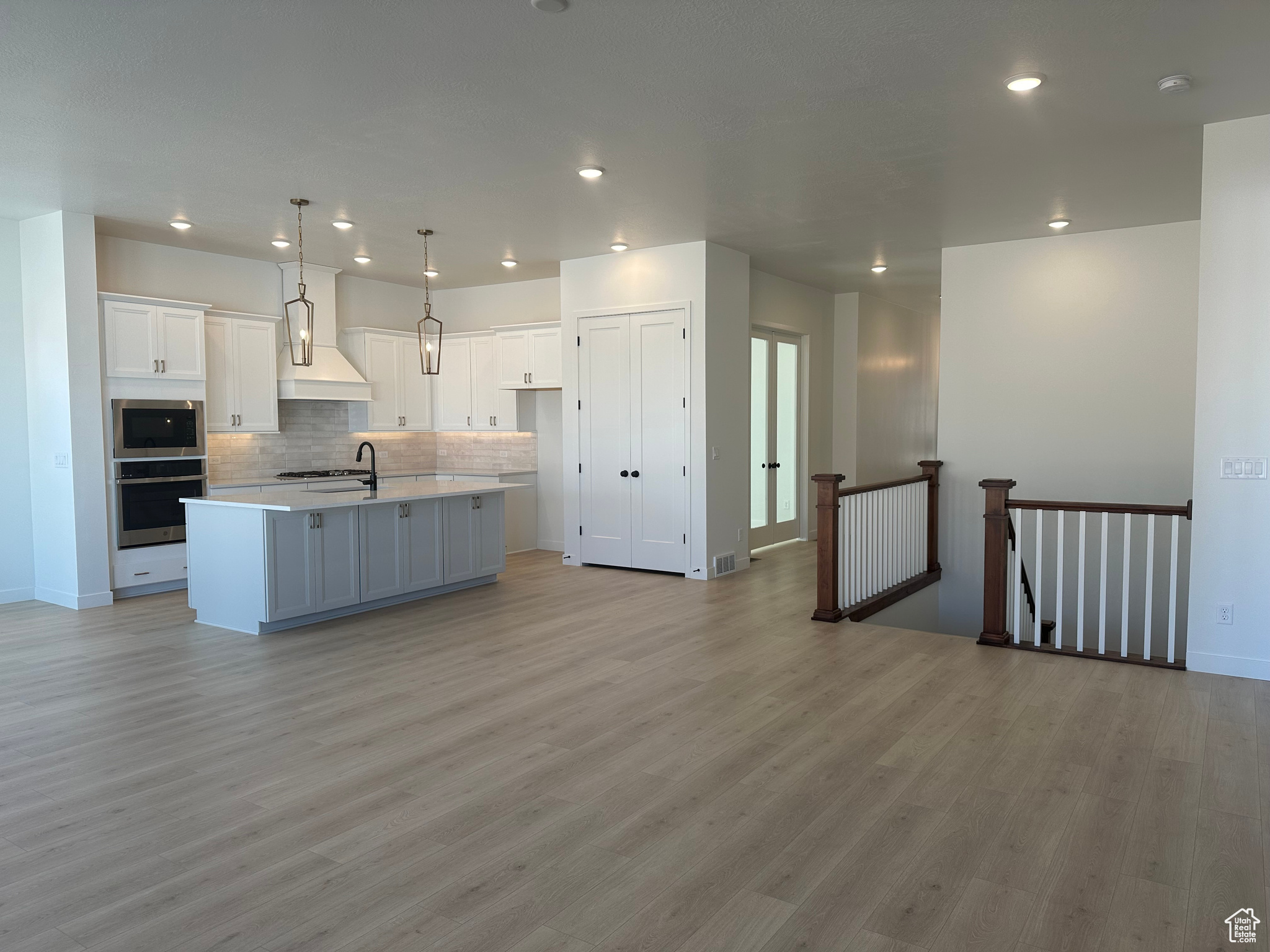 Kitchen featuring light hardwood / wood-style floors, custom exhaust hood, an island with sink, and white cabinets