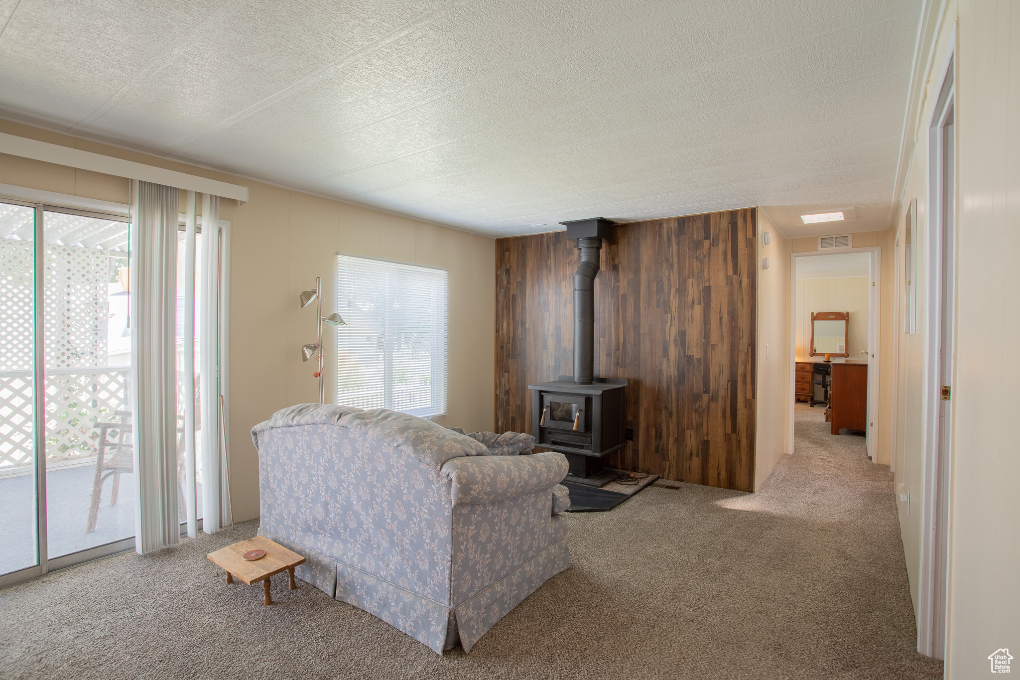 Living room with a wood stove, light colored carpet, and plenty of natural light