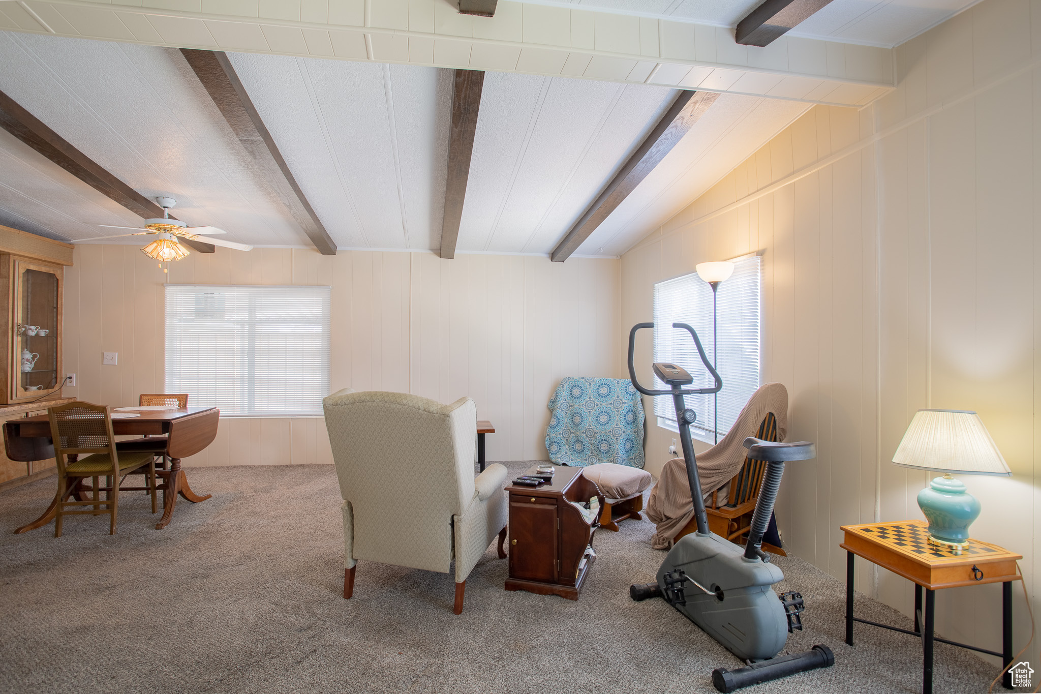 Living area featuring beamed ceiling, carpet floors, and ceiling fan