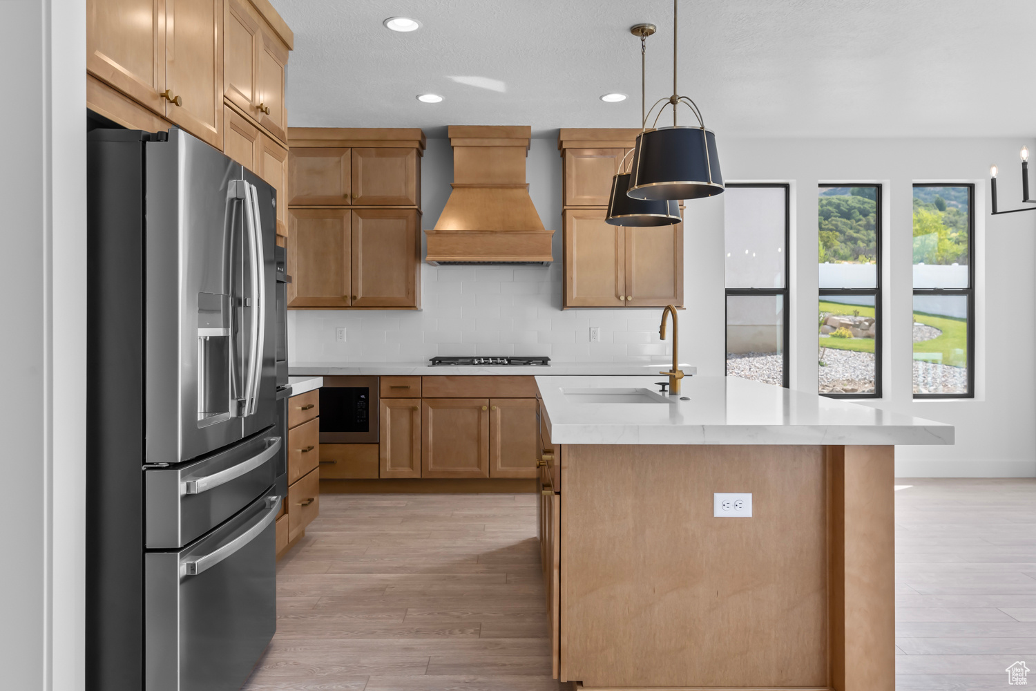 Kitchen featuring sink, hanging light fixtures, stainless steel fridge with ice dispenser, custom range hood, and a center island with sink