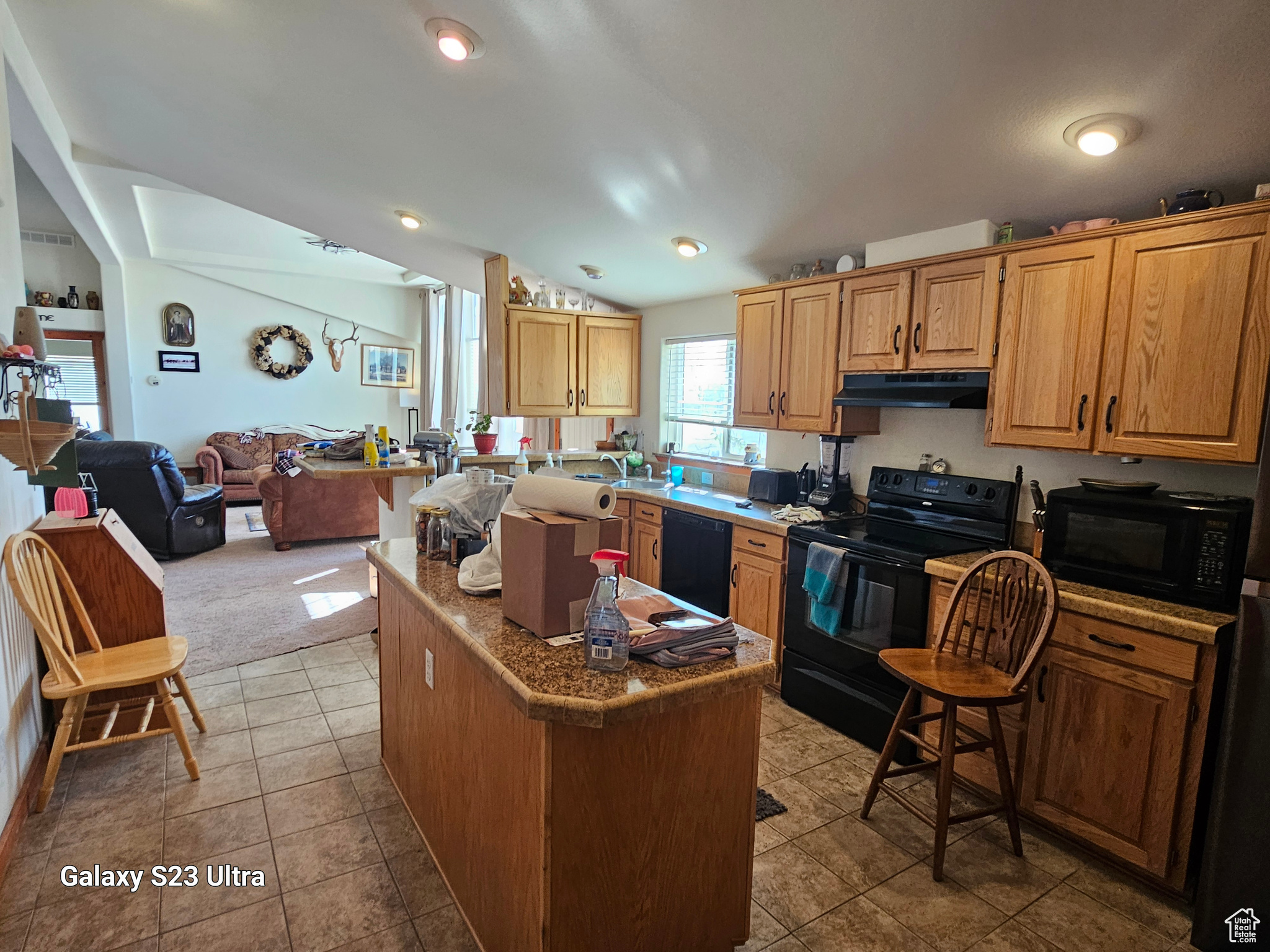 Kitchen with black appliances, vaulted ceiling, light tile patterned floors, a kitchen island, and a kitchen breakfast bar