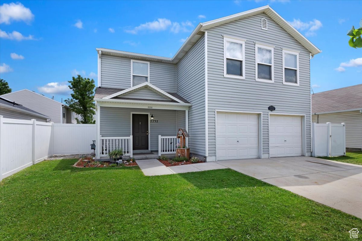 View of property featuring covered porch, a garage, and a front lawn