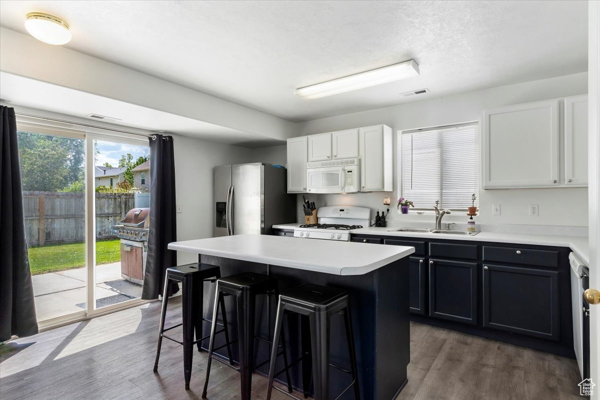 Kitchen with white cabinetry, white appliances, a kitchen island, hardwood / wood-style floors, and sink