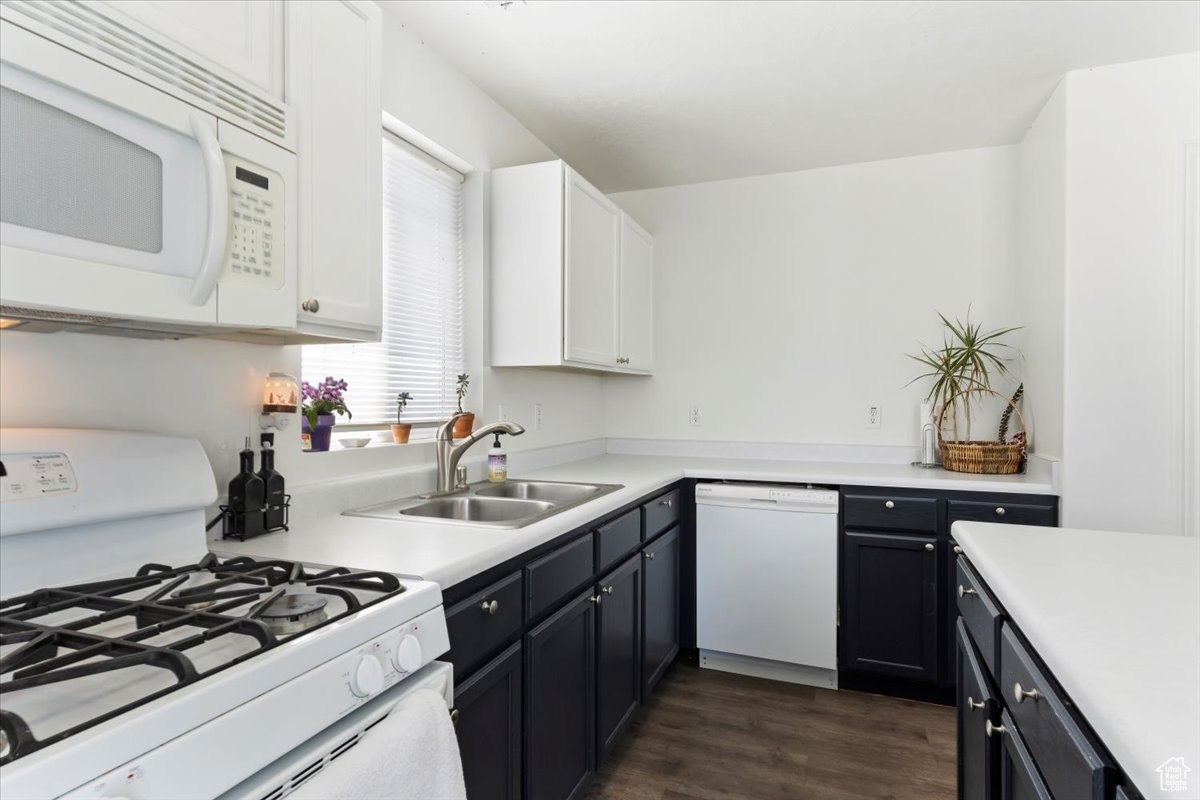 Kitchen featuring dark wood-type flooring, white cabinets, sink, and white appliances