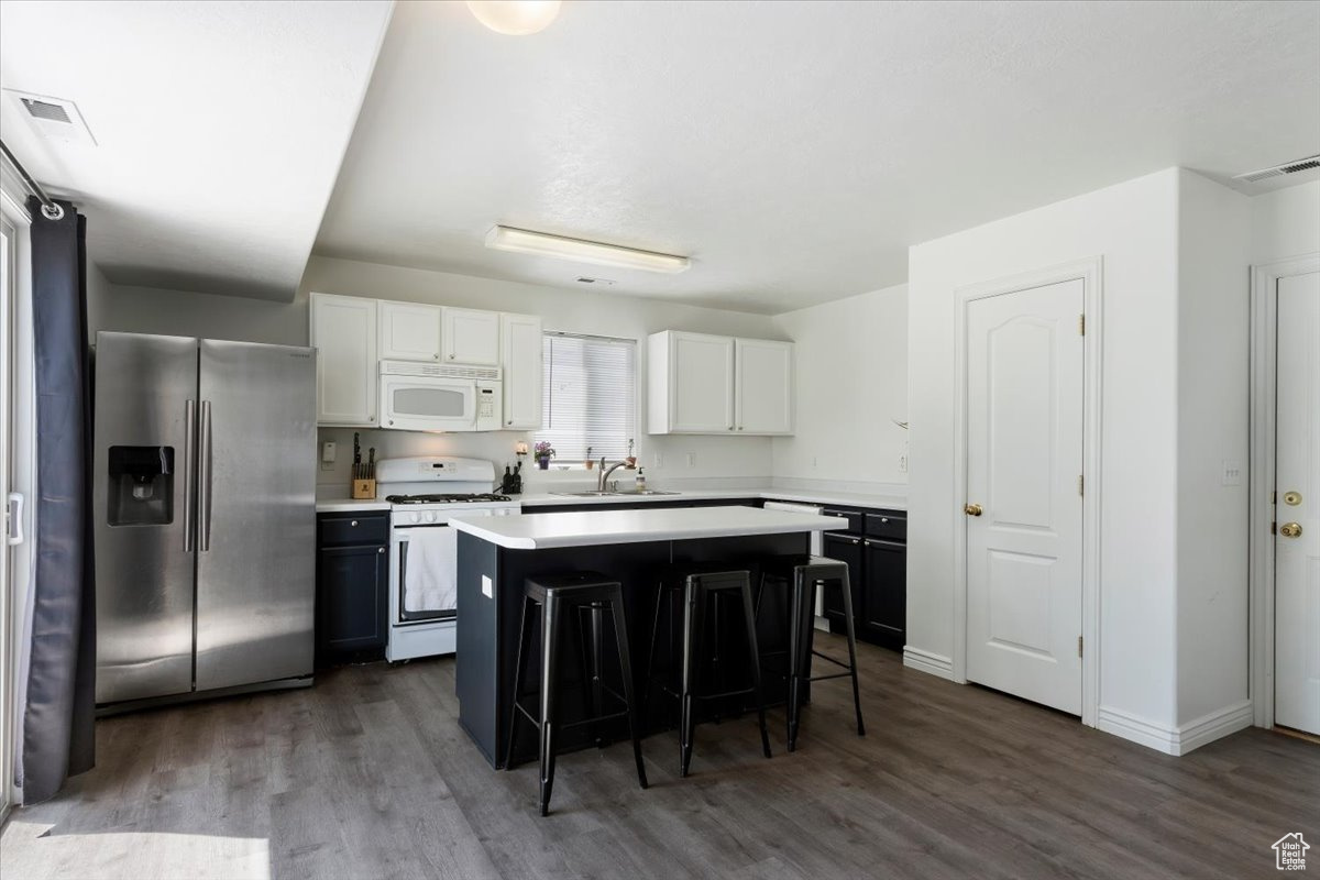 Kitchen featuring dark hardwood / wood-style flooring, white cabinets, white appliances, sink, and a kitchen island