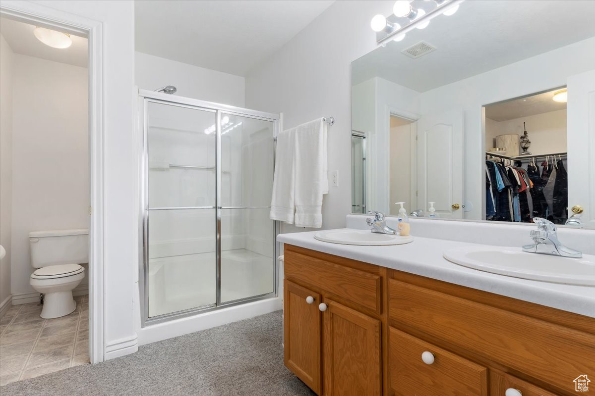 Bathroom with a shower with shower door, double vanity, tile patterned floors, and toilet