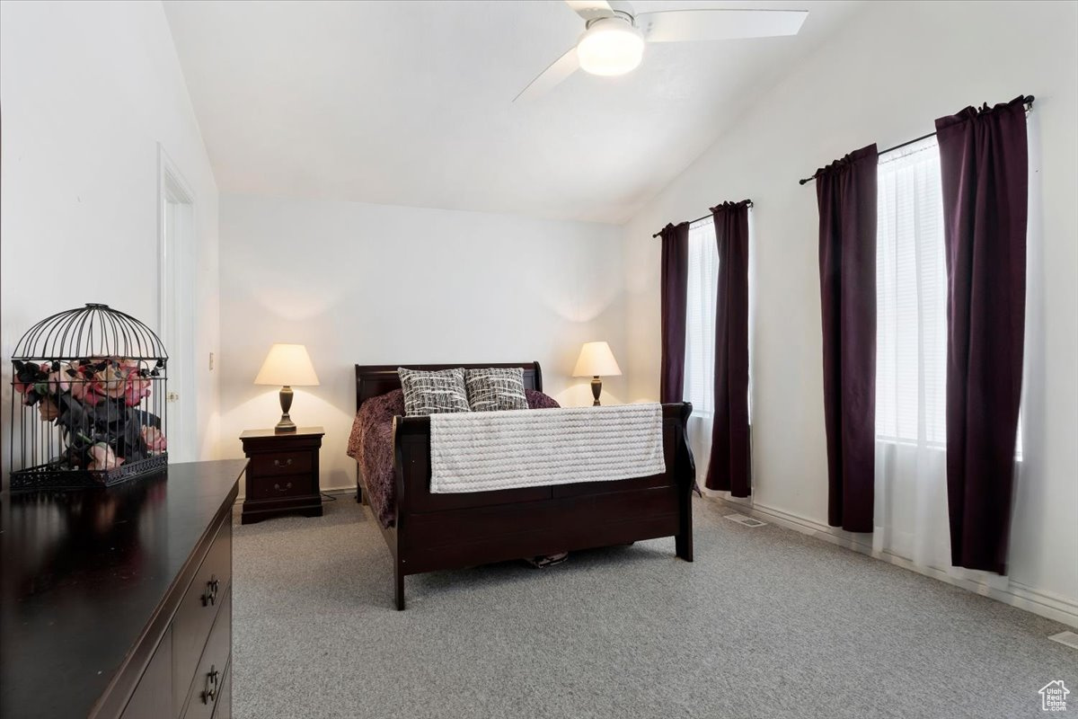 Bedroom with light carpet, ceiling fan, and vaulted ceiling