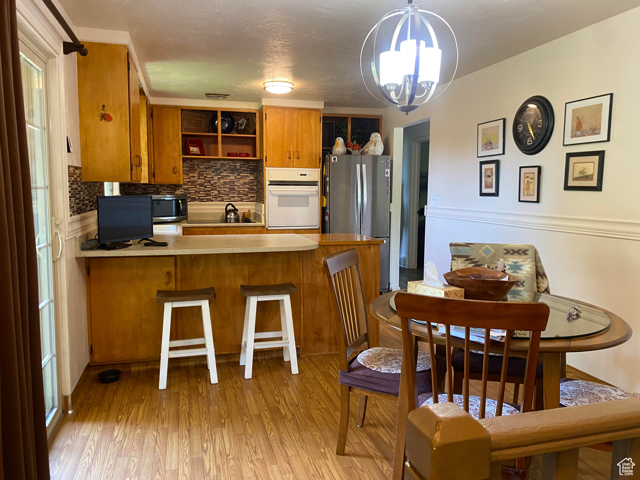 Kitchen with a notable chandelier, appliances with stainless steel finishes, light hardwood flooring, kitchen peninsula, and backsplash