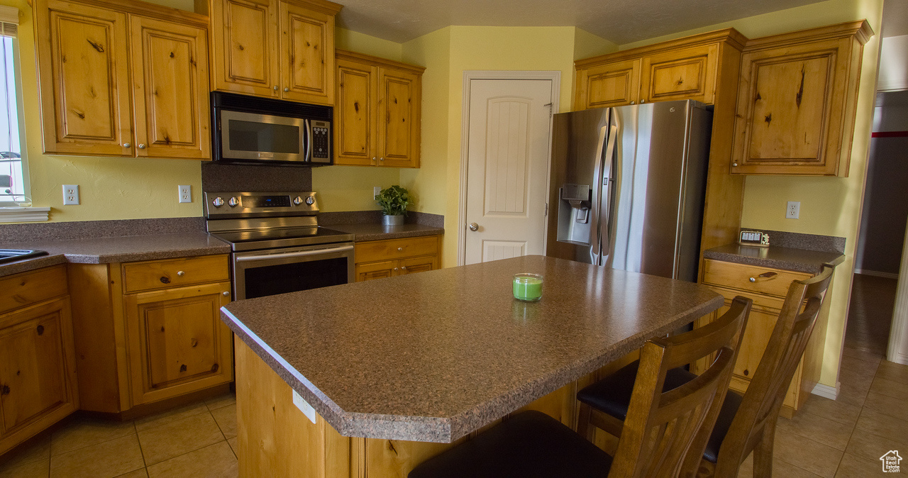 Kitchen featuring appliances with stainless steel finishes, light tile patterned floors, and a kitchen island