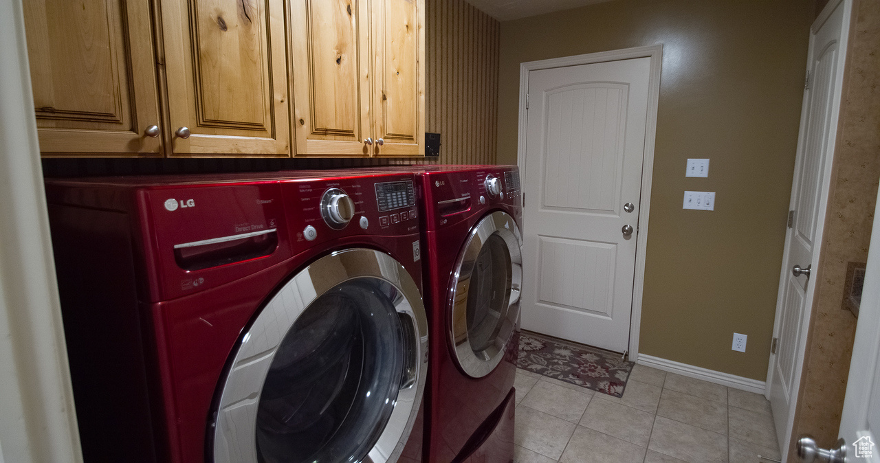 Washroom featuring light tile patterned floors, washer and clothes dryer, and cabinets