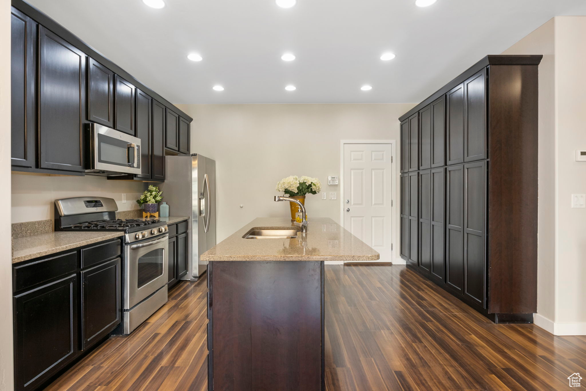 Kitchen with stainless steel appliances, a center island with sink, light stone counters, and dark hardwood / wood-style flooring