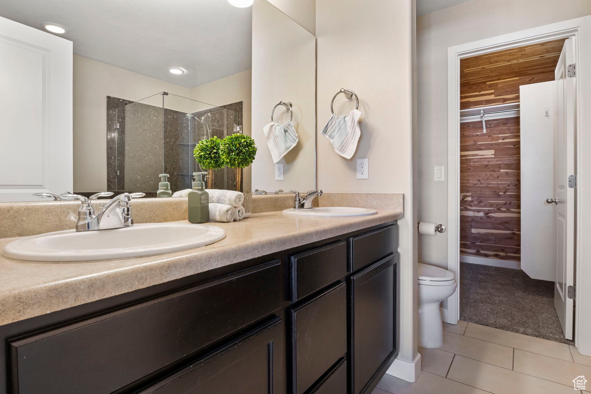 Bathroom featuring tile patterned flooring, a tile shower, toilet, and dual bowl vanity