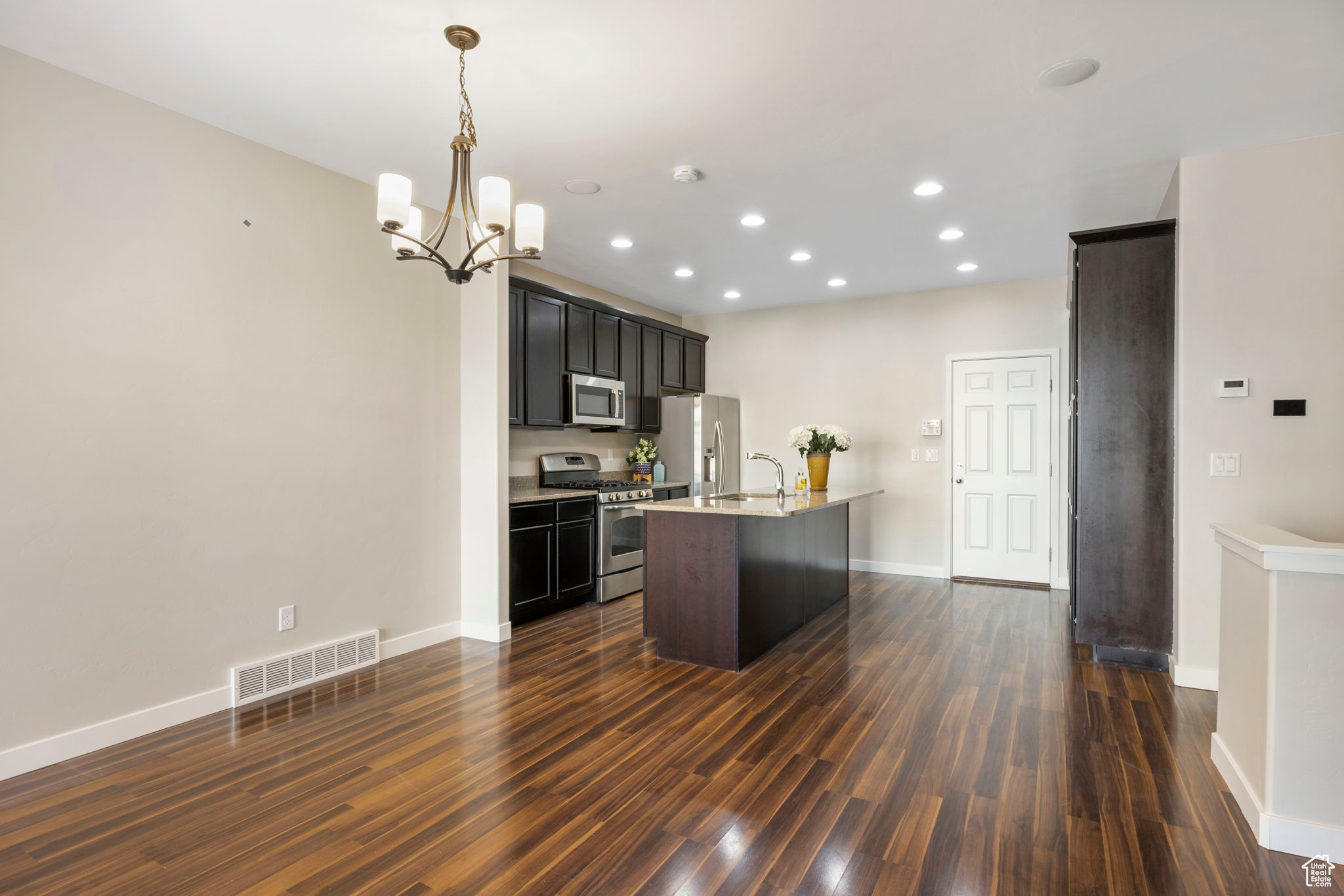 Kitchen with decorative light fixtures, an island with sink,  appliances with stainless steel finishes, and dark wood-type flooring