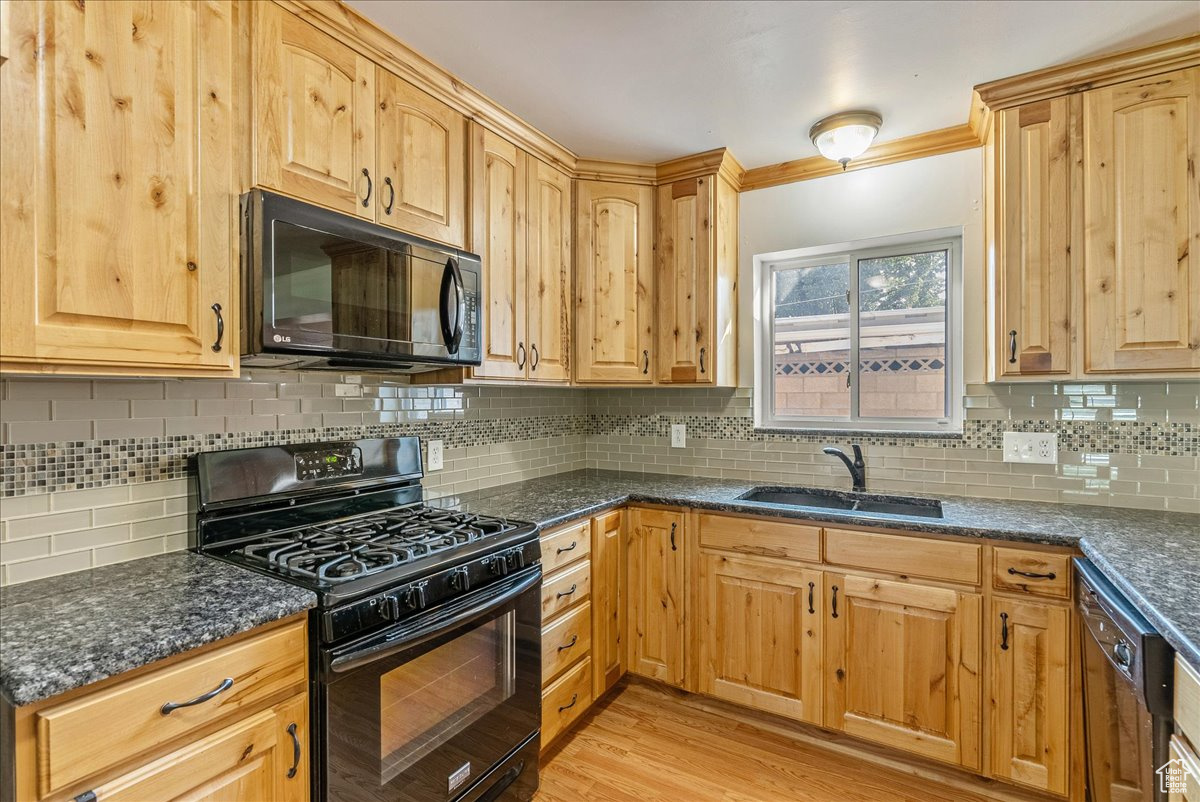 Kitchen featuring black appliances, crown molding, sink, light hardwood / wood-style floors, and backsplash