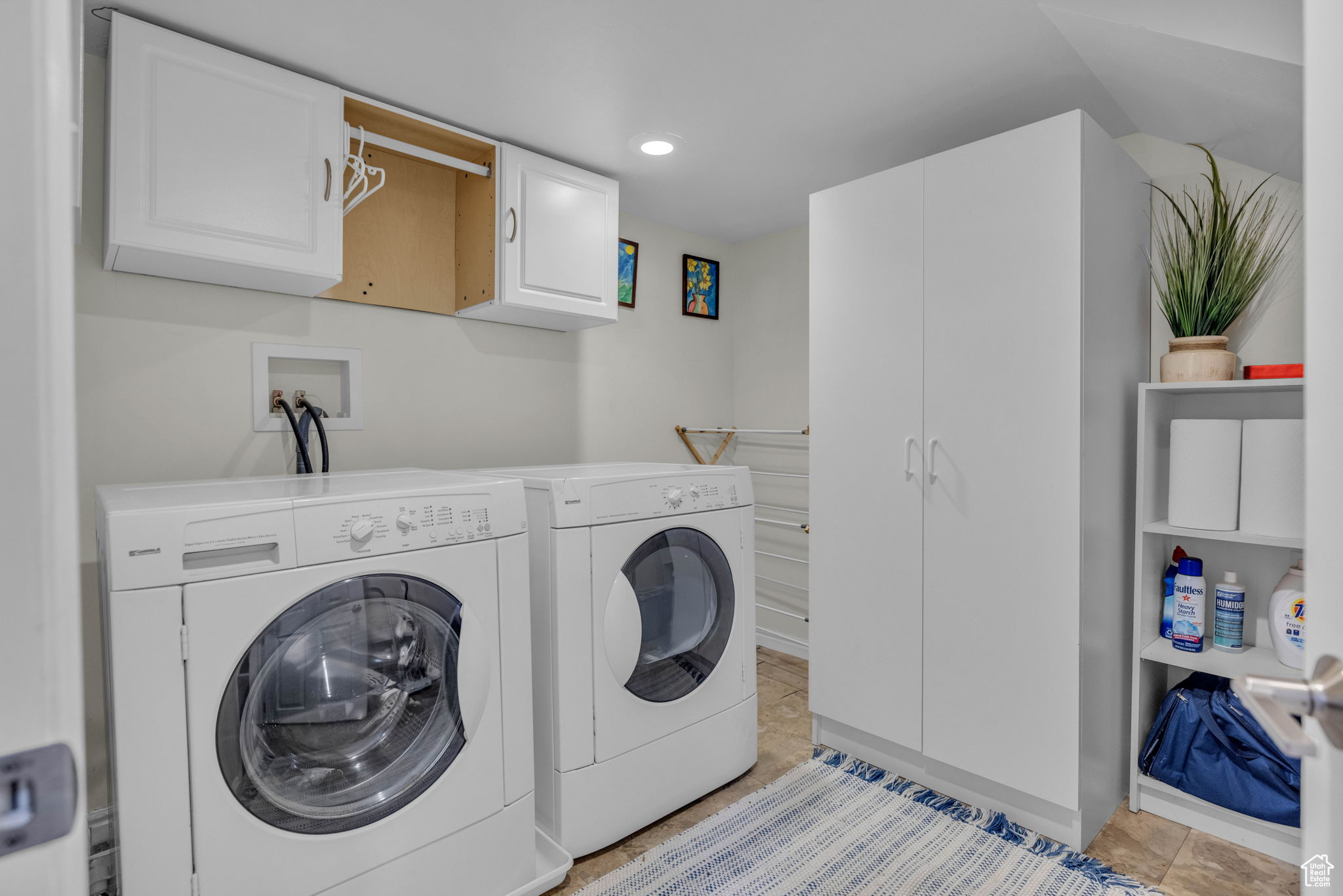 Clothes washing area with cabinets, light tile patterned floors, and washer and clothes dryer