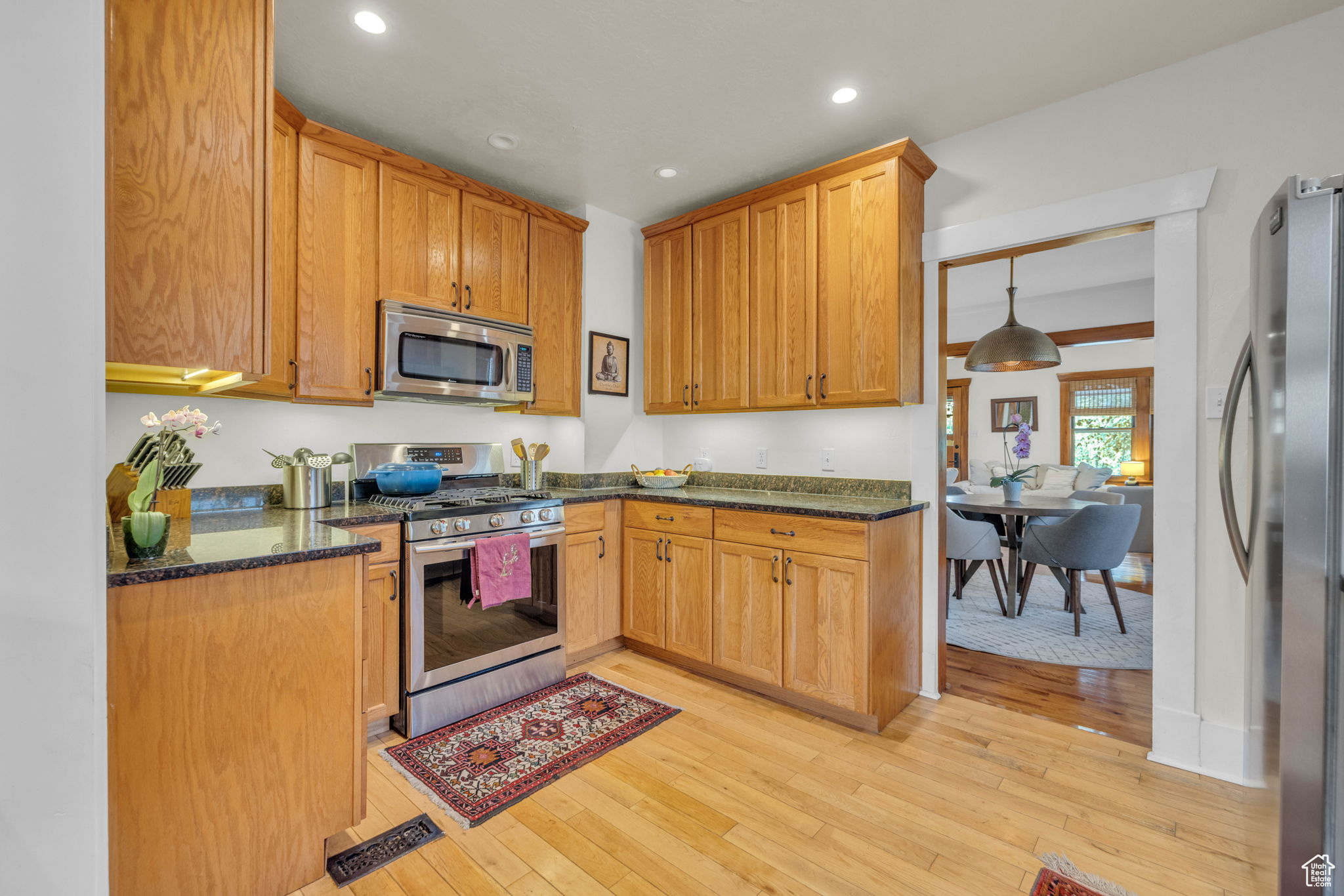 Kitchen with light wood-type flooring, stainless steel appliances, and dark stone countertops