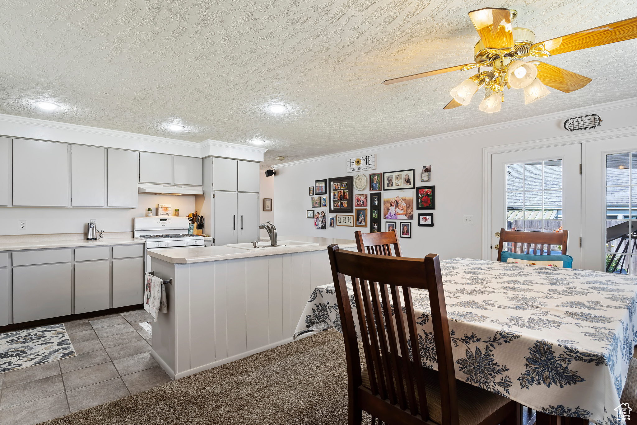 Kitchen featuring a textured ceiling, crown molding, light tile patterned flooring, ceiling fan, and sink