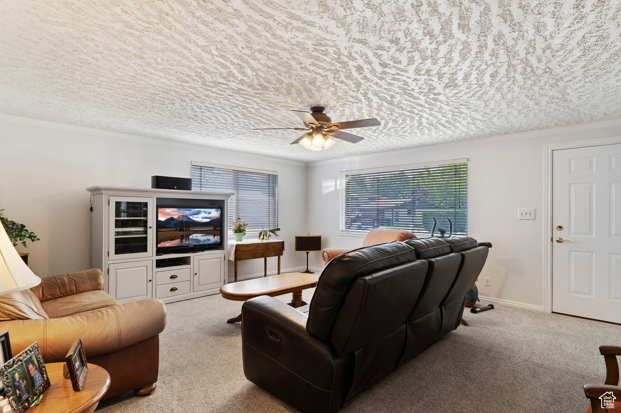 Living room featuring ceiling fan, a textured ceiling, ornamental molding, and light carpet