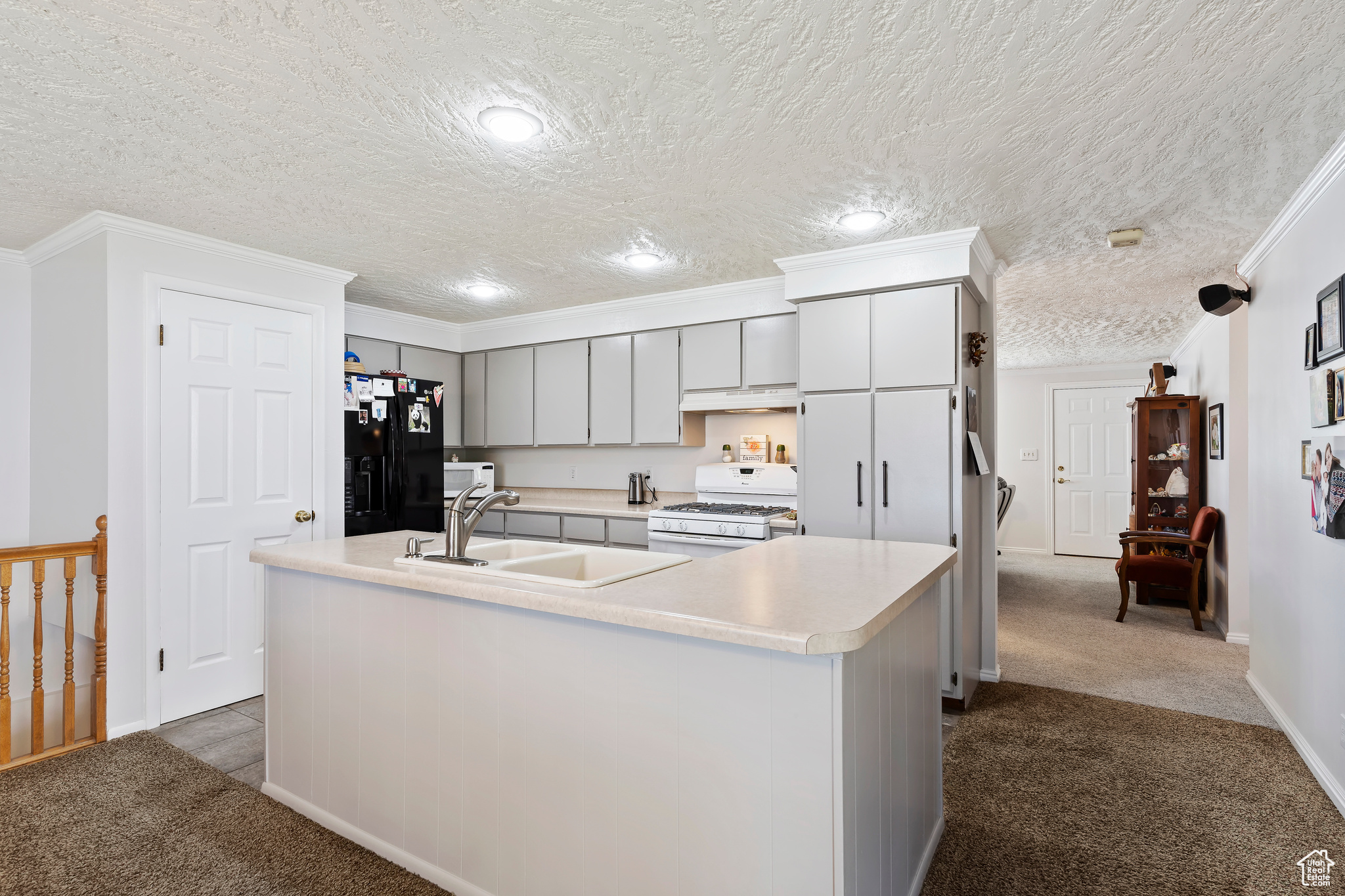 Kitchen featuring crown molding, dark carpet, a center island with sink, white appliances, and sink