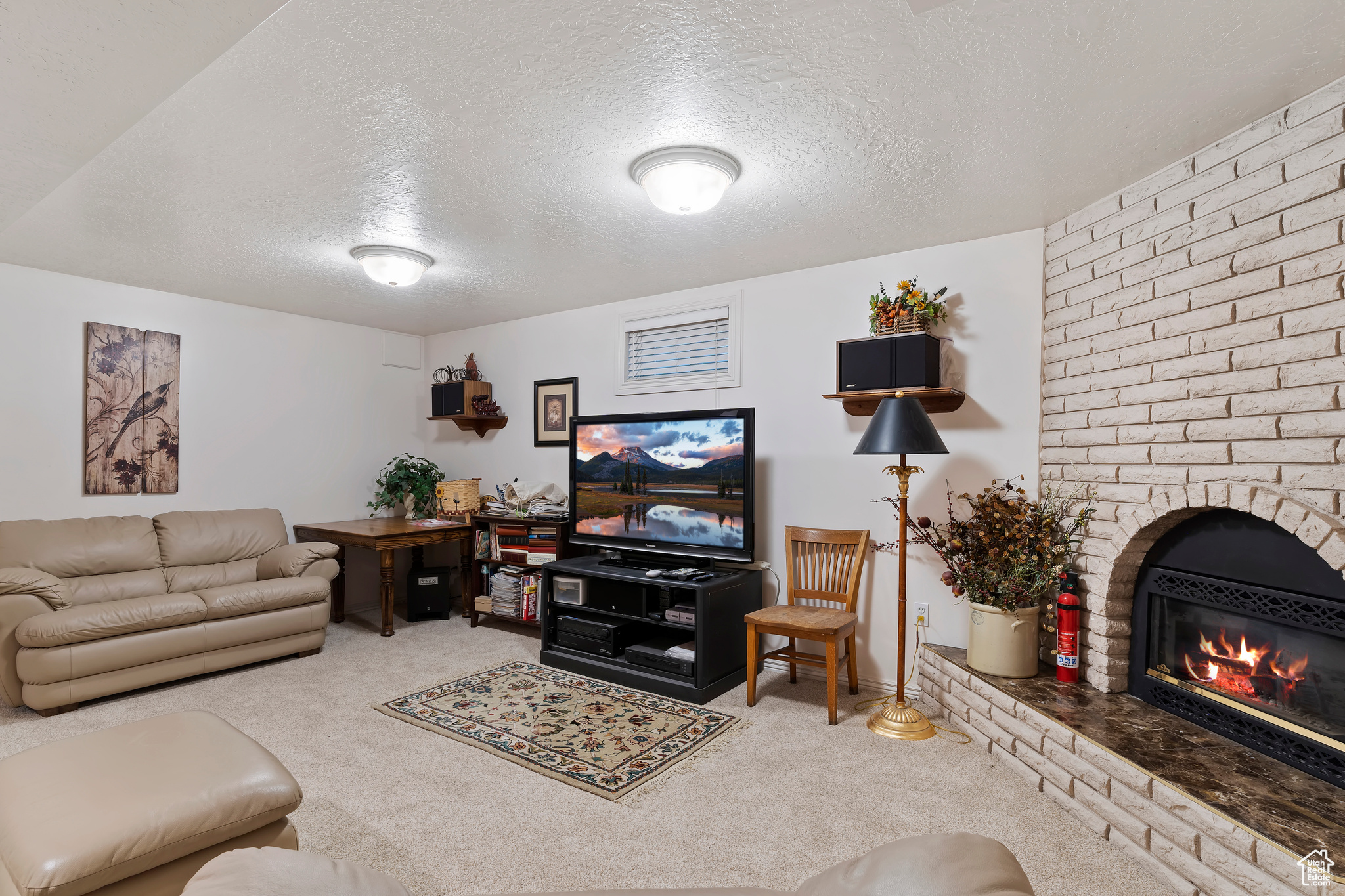 Carpeted living room featuring brick wall, a textured ceiling, and a brick fireplace