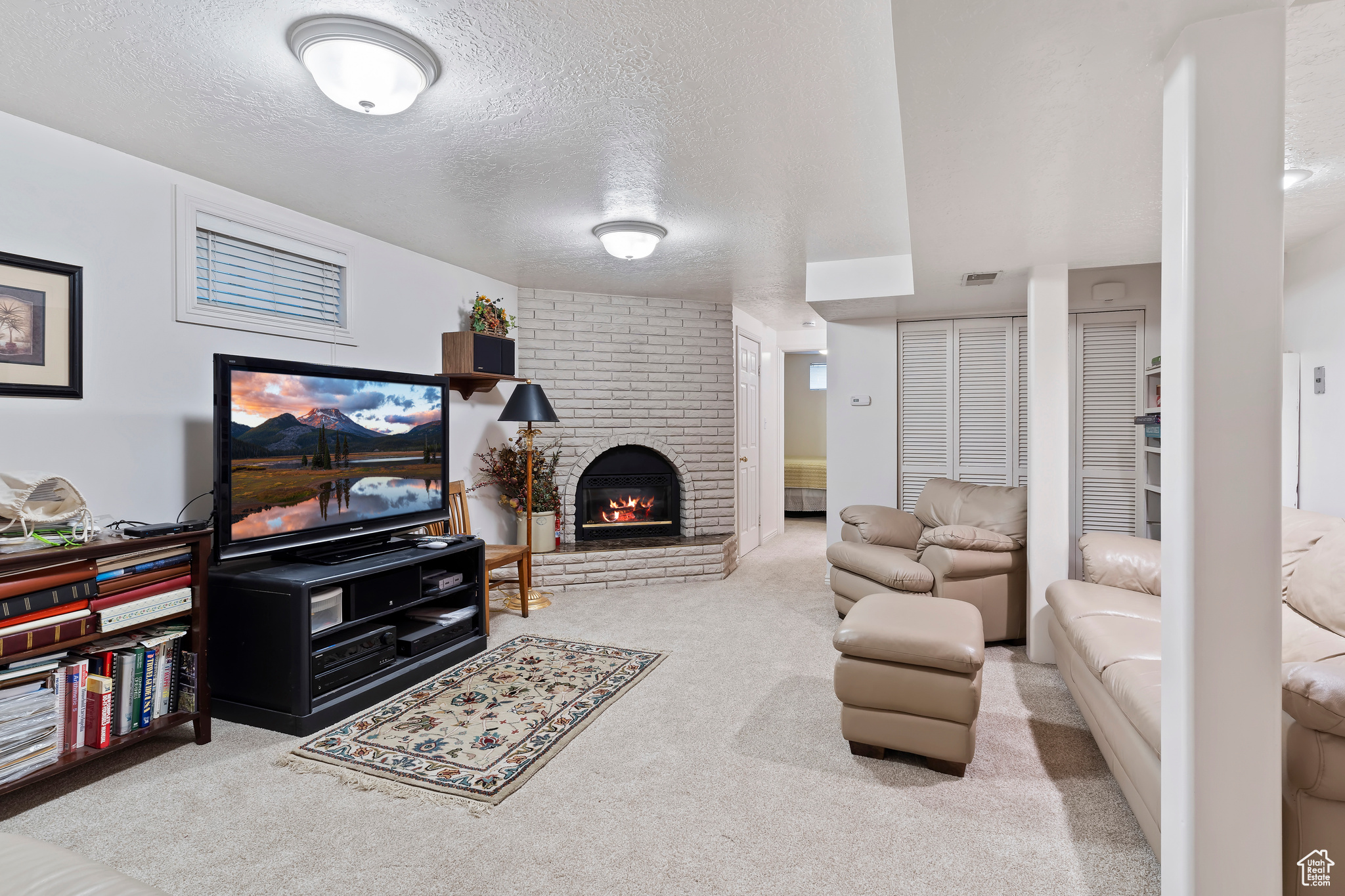 Living room with a fireplace, a textured ceiling, light colored carpet, and brick wall