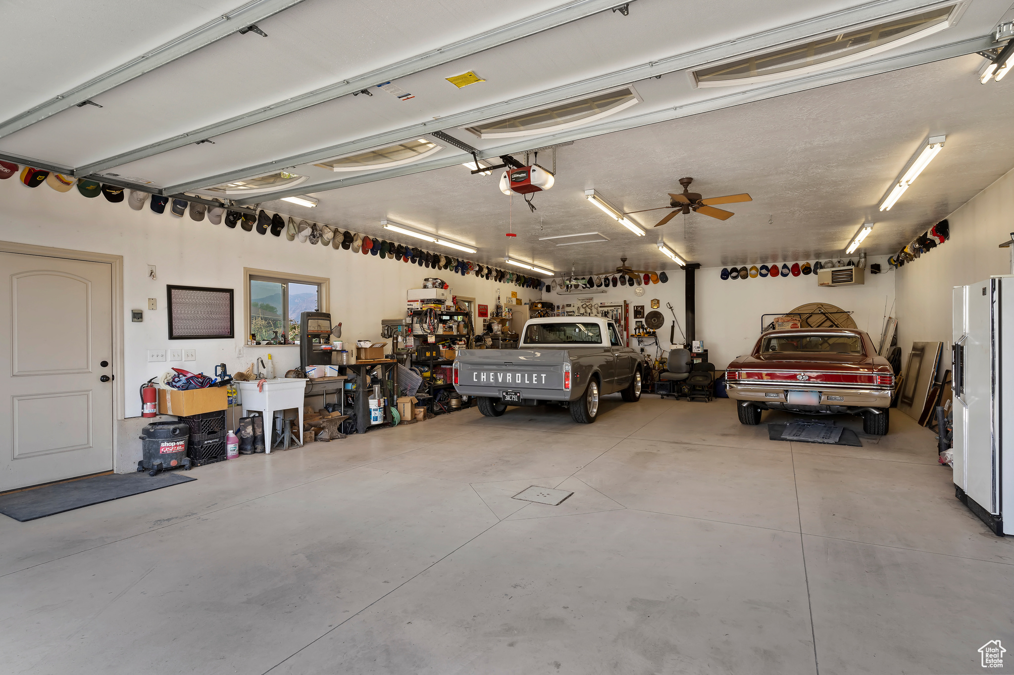 Garage with a garage door opener, a workshop area, ceiling fan, and white fridge