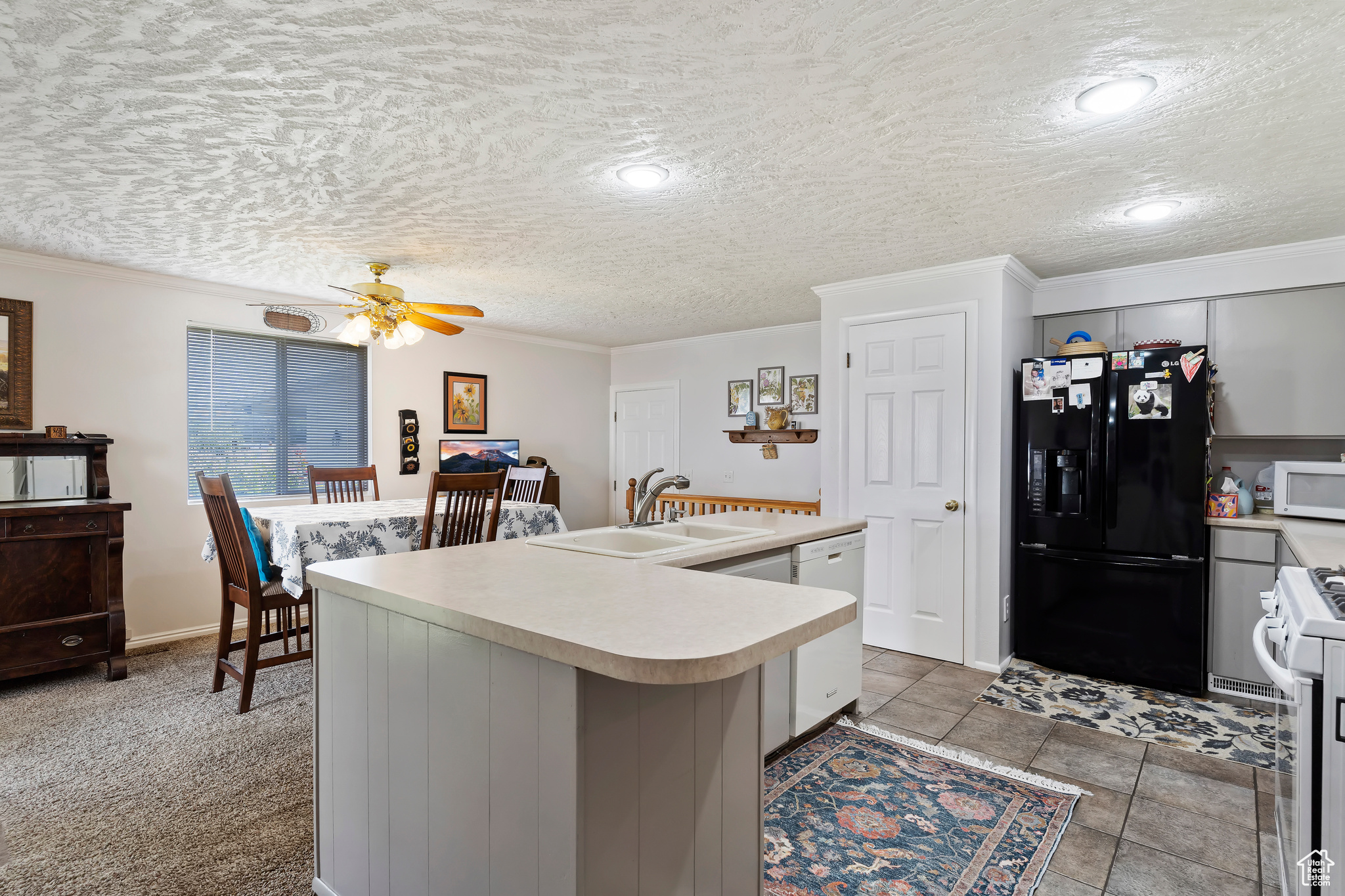 Kitchen with white appliances, light tile patterned flooring, a kitchen island with sink, ceiling fan, and sink