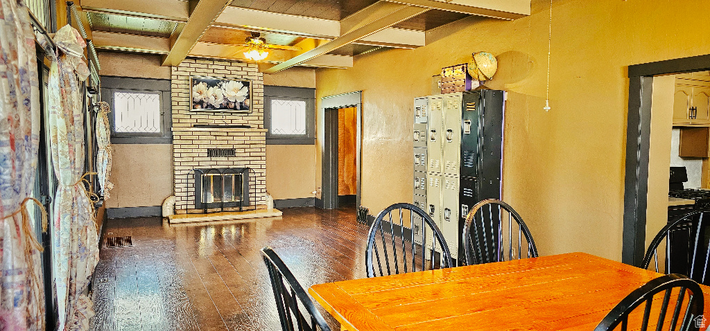 Dining room with beamed ceiling, a brick fireplace, ceiling fan, and dark wood-type flooring