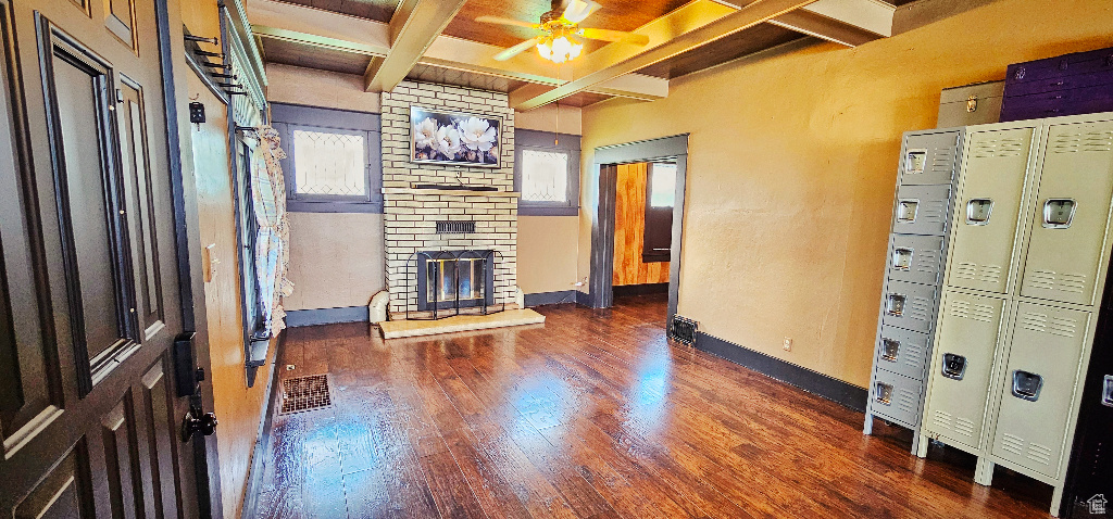 Unfurnished living room with a fireplace, beam ceiling, dark wood-type flooring, and ceiling fan