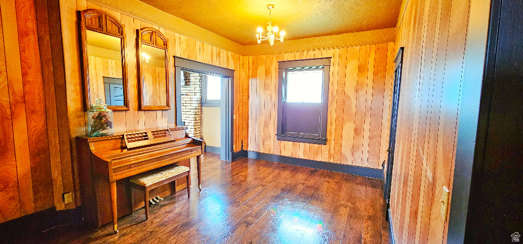 Miscellaneous room with a chandelier, a textured ceiling, dark hardwood / wood-style floors, and wooden walls