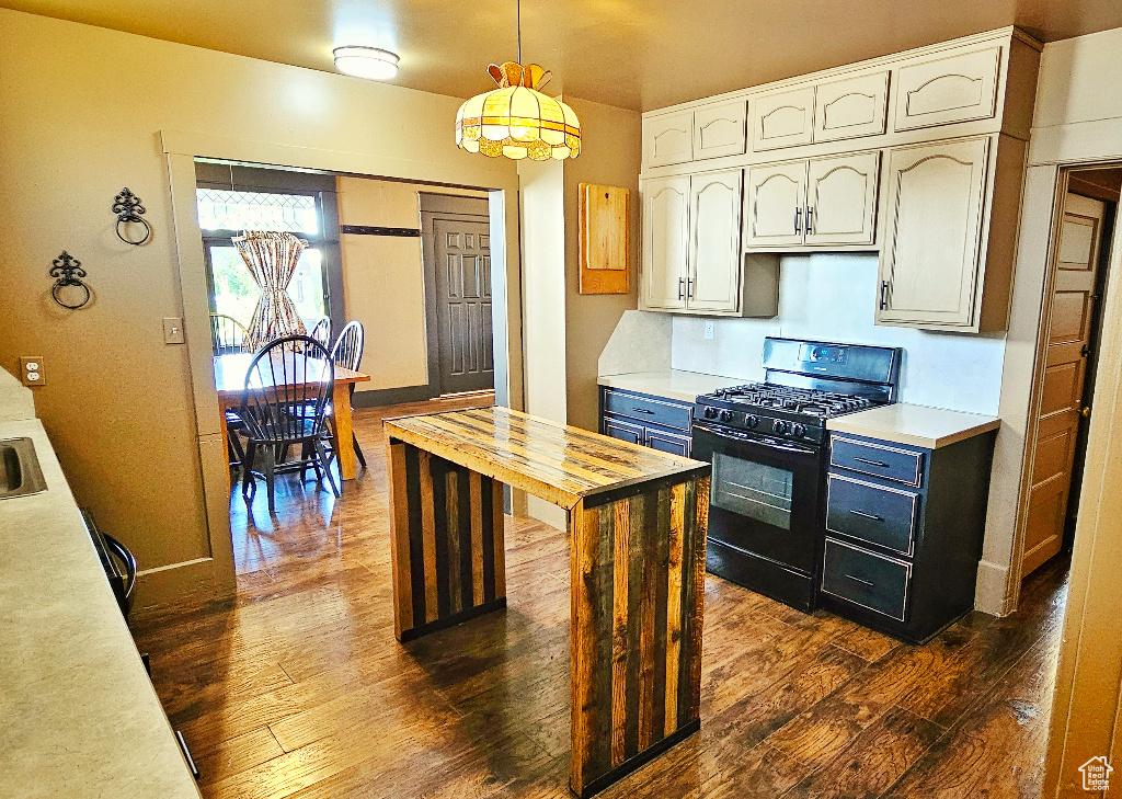 Kitchen featuring dark hardwood / wood-style flooring, white cabinets, decorative light fixtures, and black gas range oven