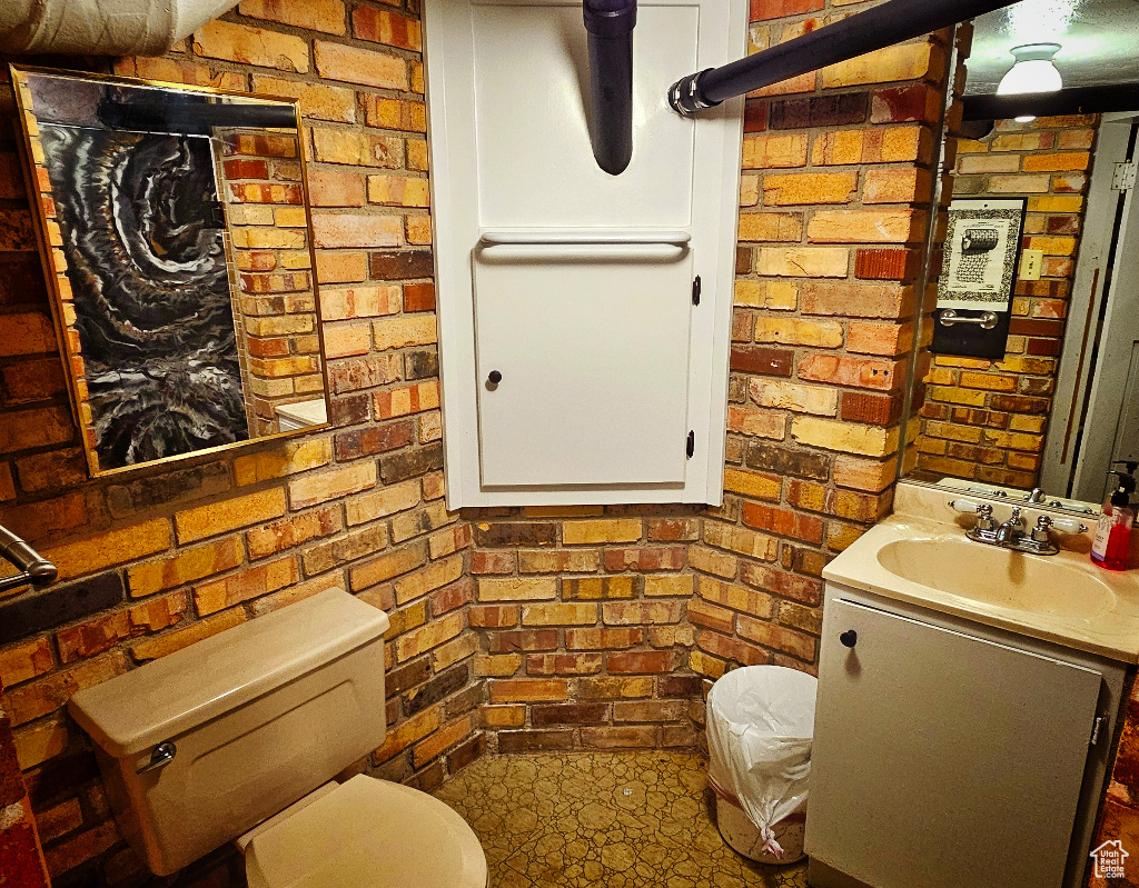 Bathroom with vanity, toilet, and brick wall