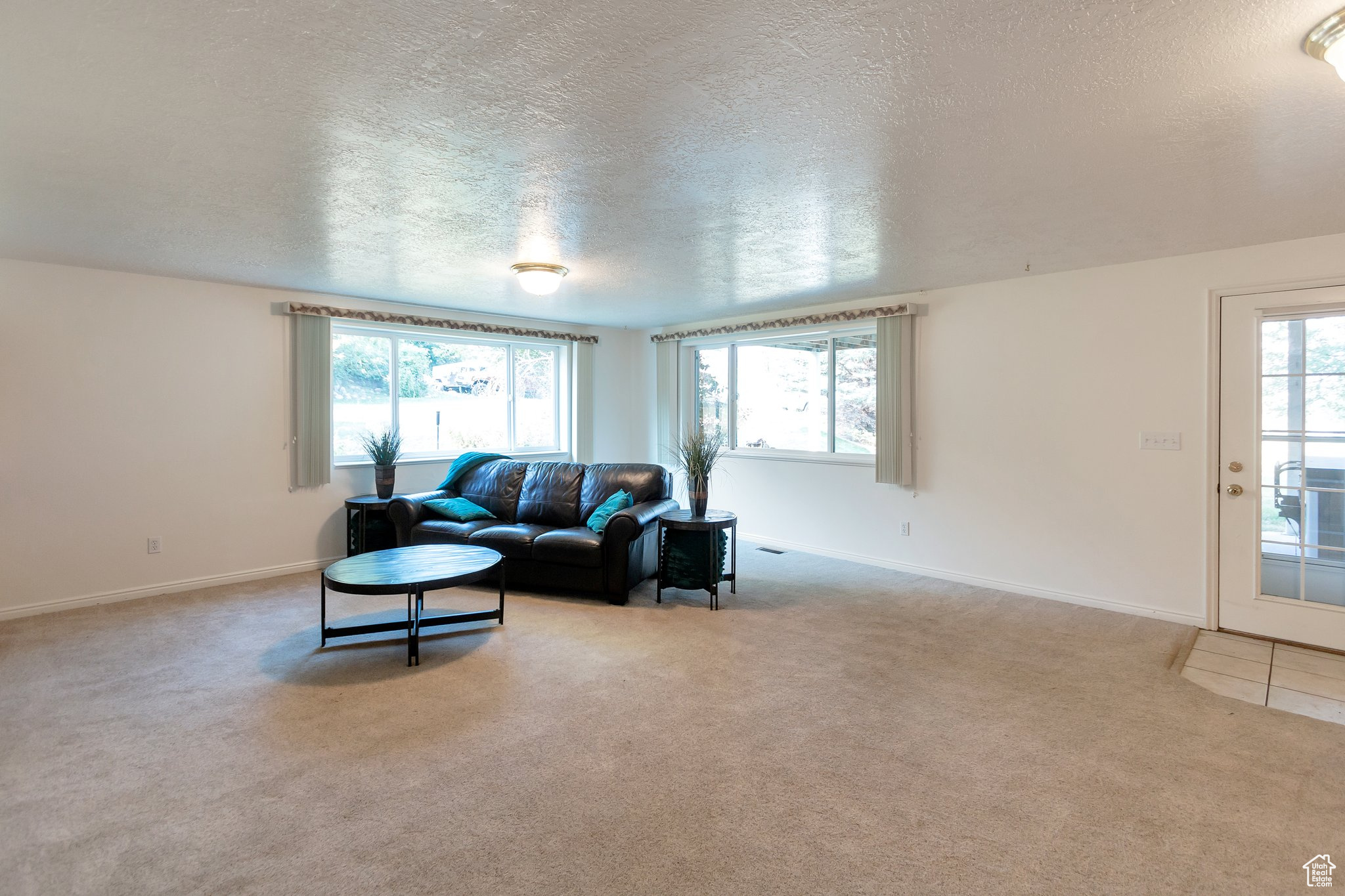 Living room with a textured ceiling, light colored carpet, and a wealth of natural light