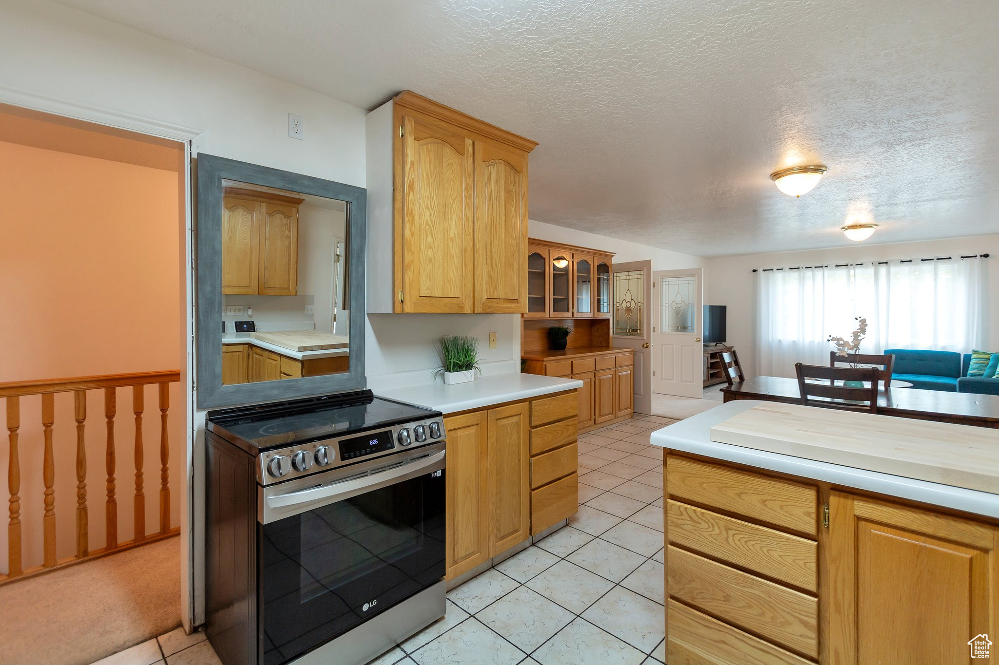 Kitchen featuring light tile patterned flooring, a textured ceiling, light brown cabinets, and stainless steel range with electric cooktop