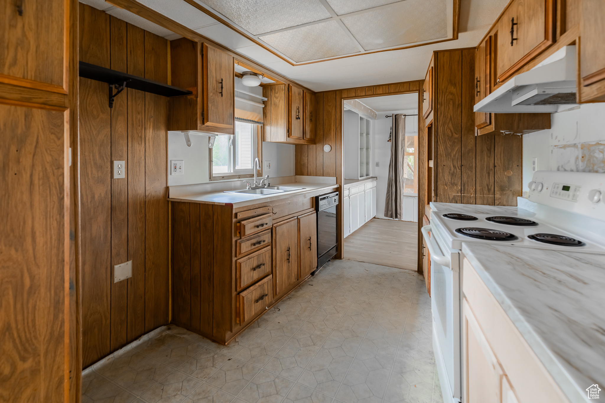 Kitchen with light tile patterned floors, white electric range, wooden walls, and sink