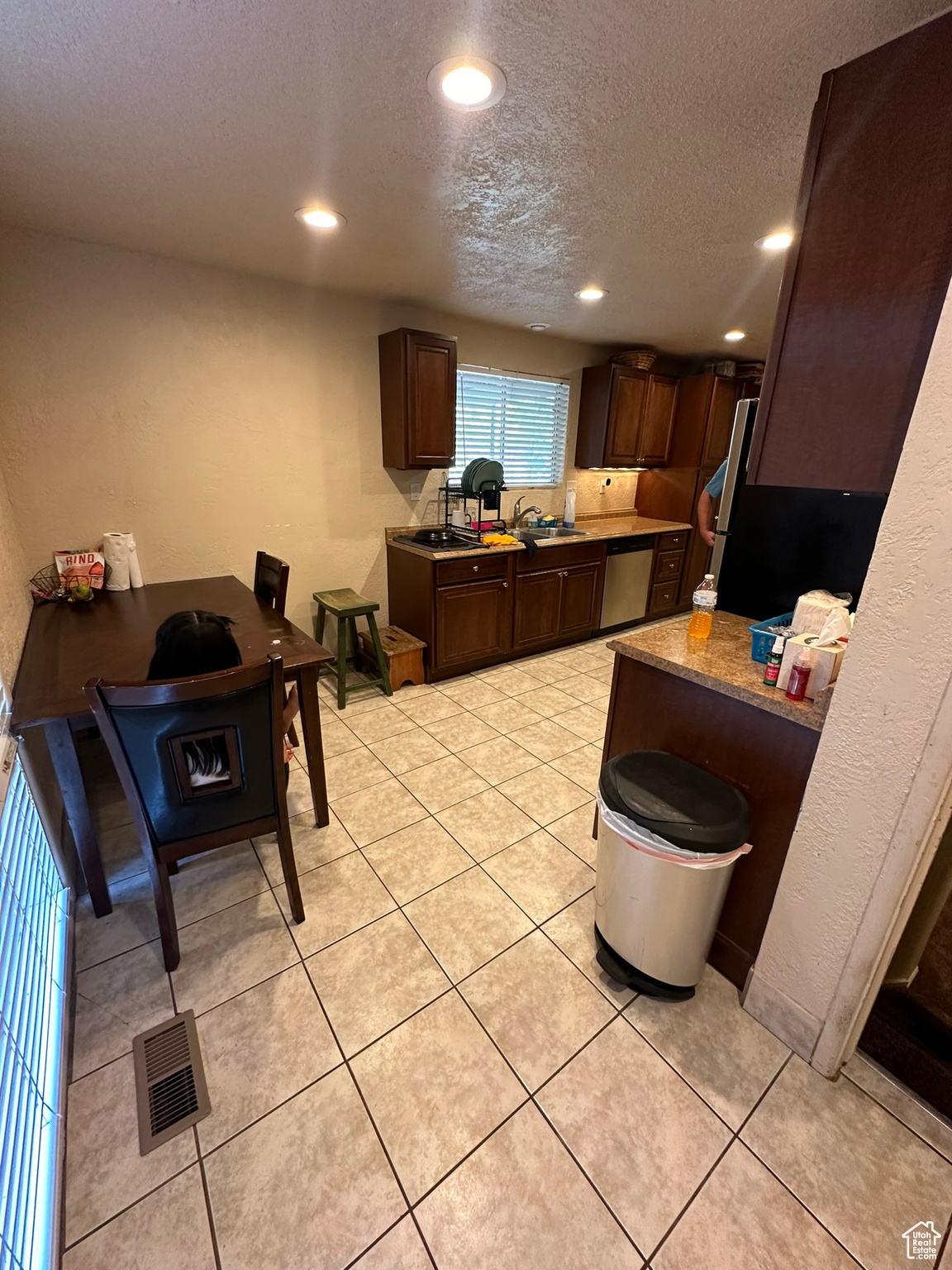 Kitchen featuring a textured ceiling, dishwasher, dark brown cabinetry, light tile floors, and sink